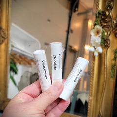 Lip balms in white tubes with flavor labels held in hand near mirror frame