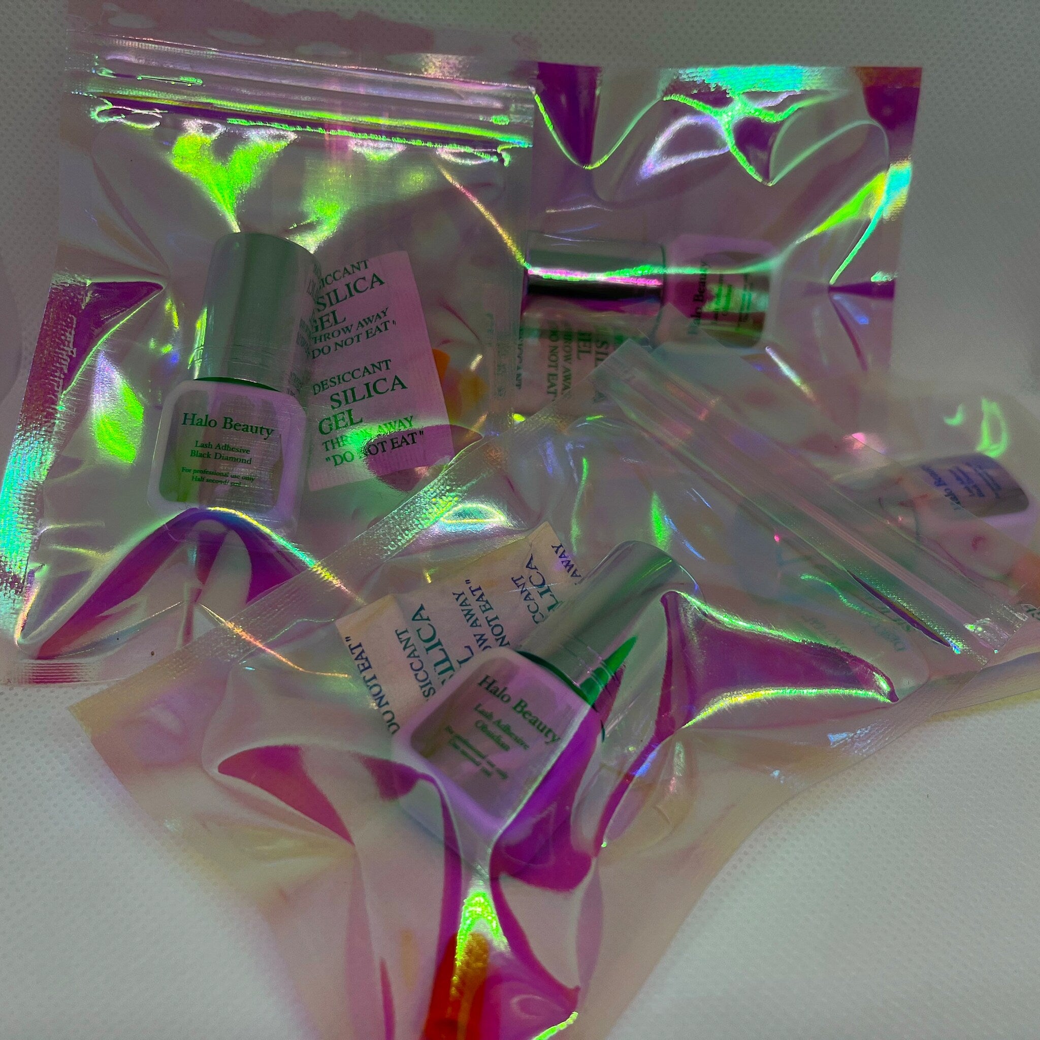 Lash adhesive bottles in iridescent plastic packaging with Halo Beauty brand text visible