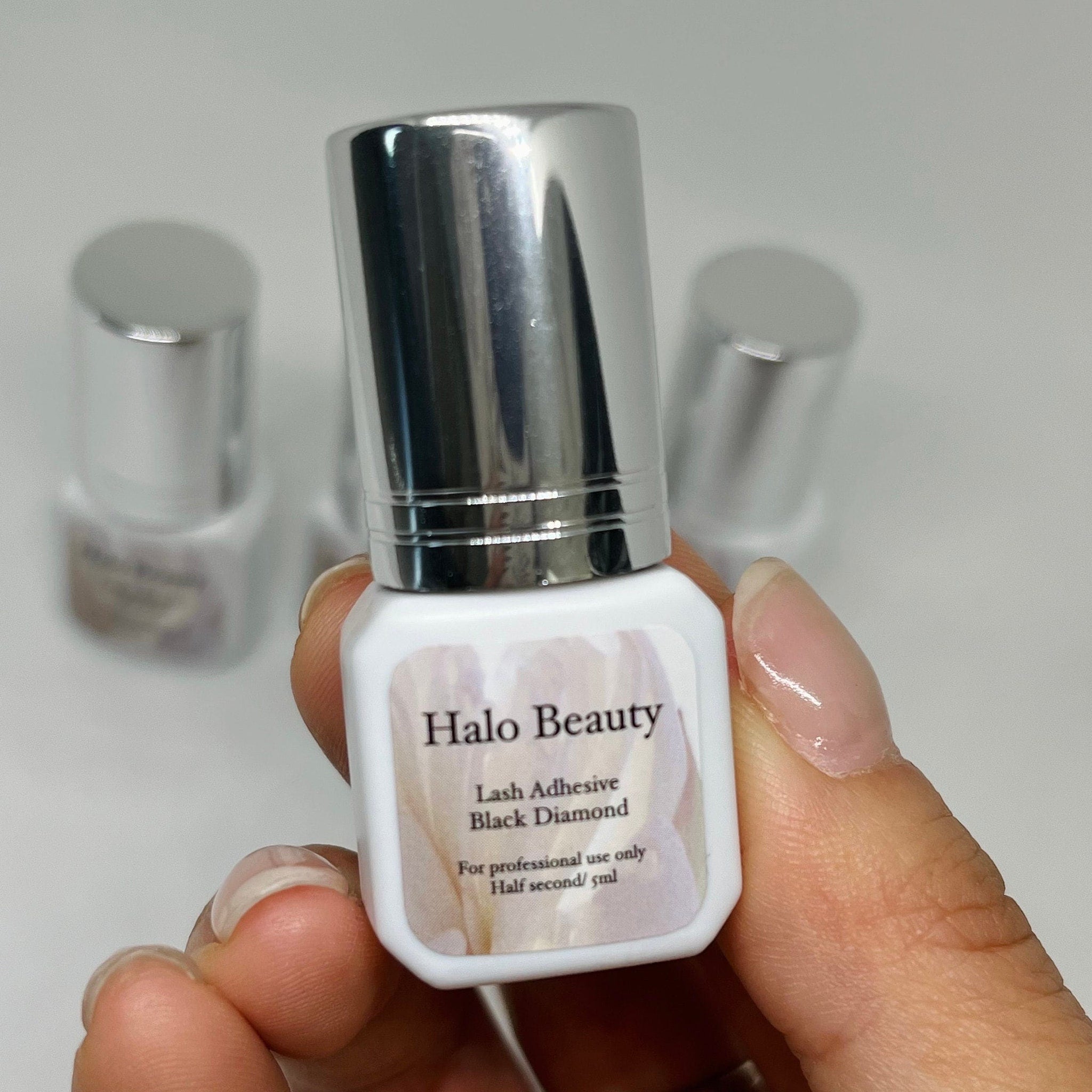 Lash adhesive bottle with silver cap, white label, and Halo Beauty text, held in hand