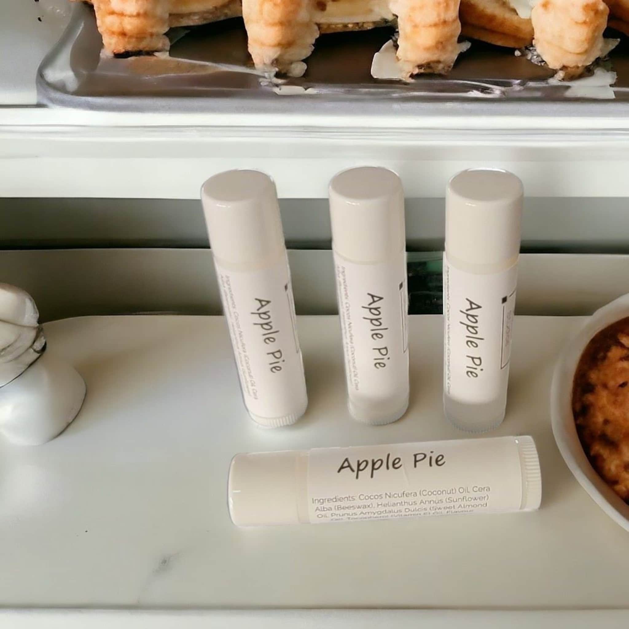 Lip balm tubes, white with "Apple Pie" text, on white surface with food nearby