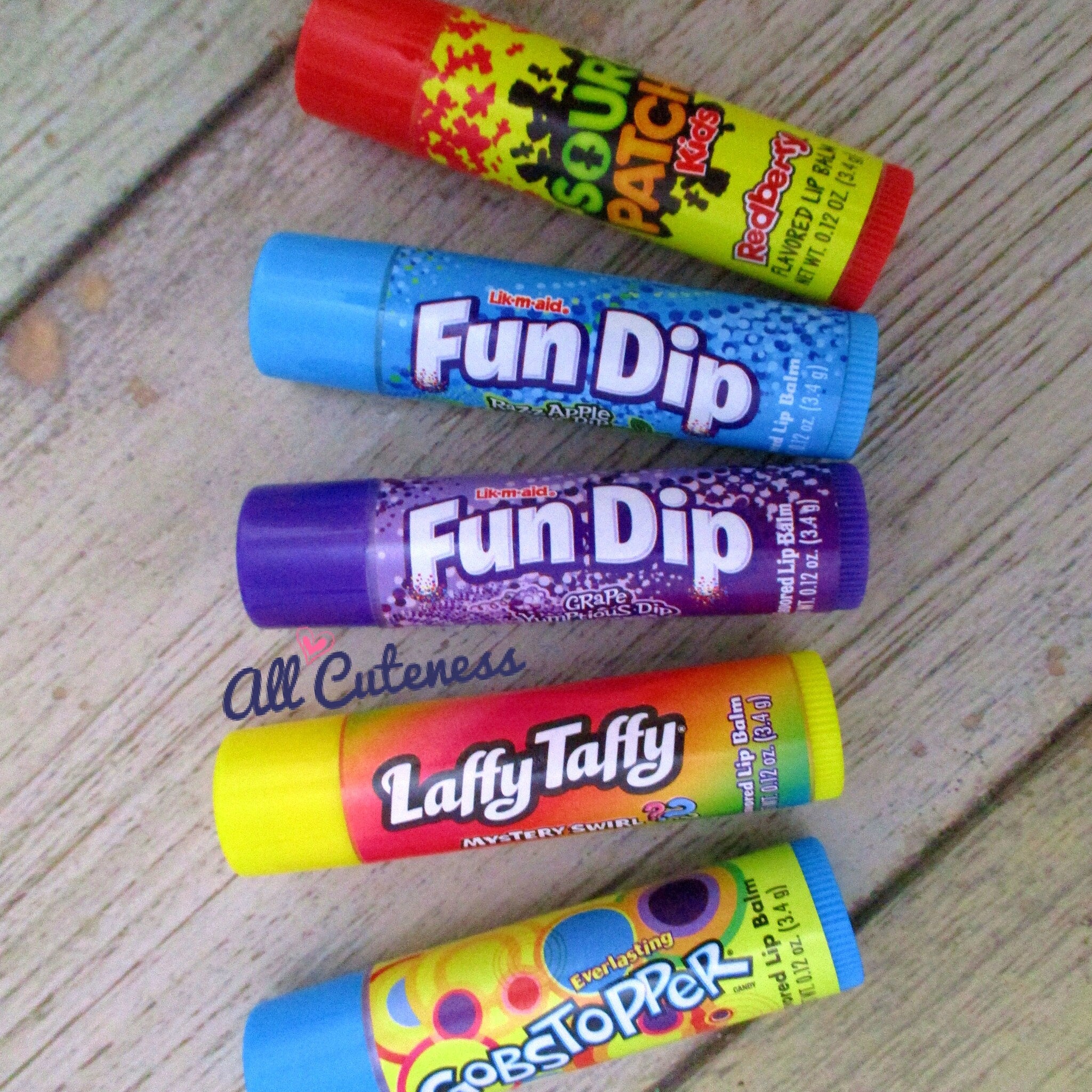 Lip balm tubes in red, blue, purple, and yellow with text and patterns on wood background