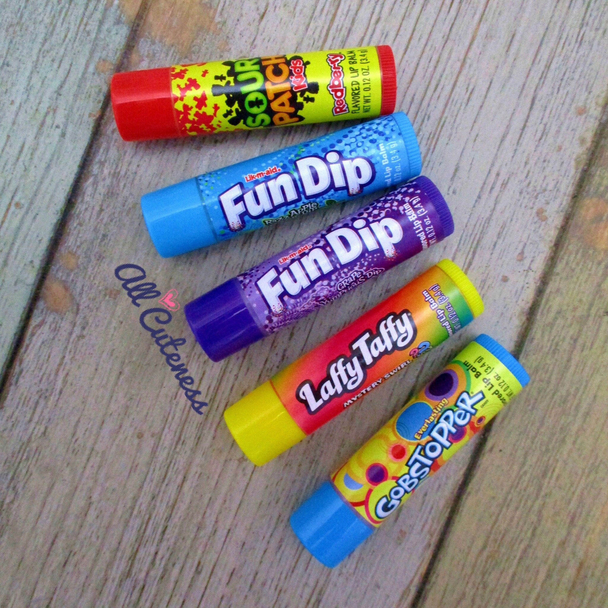 Lip balm tubes in various colors with brand names on a wooden surface.