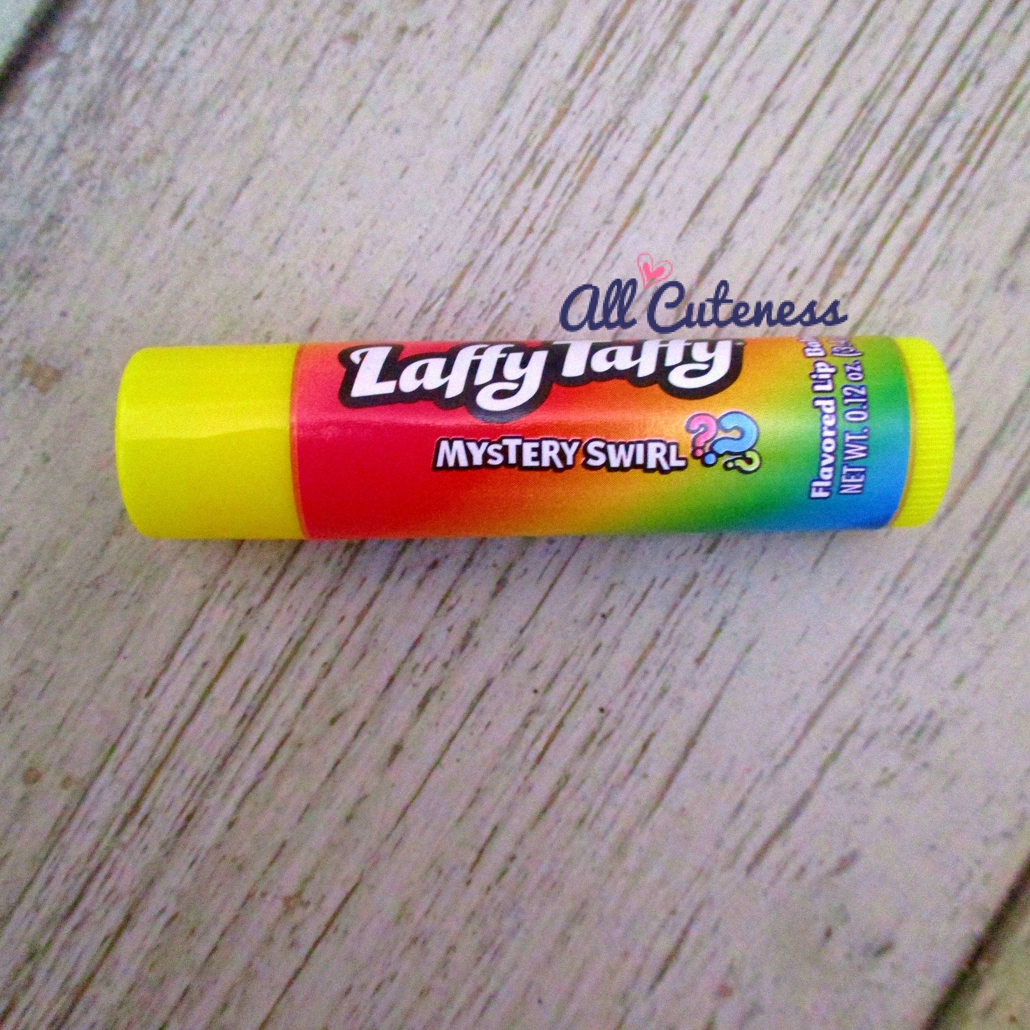 Laffy Taffy lip balm with yellow, red, and rainbow colors, on a wooden surface.