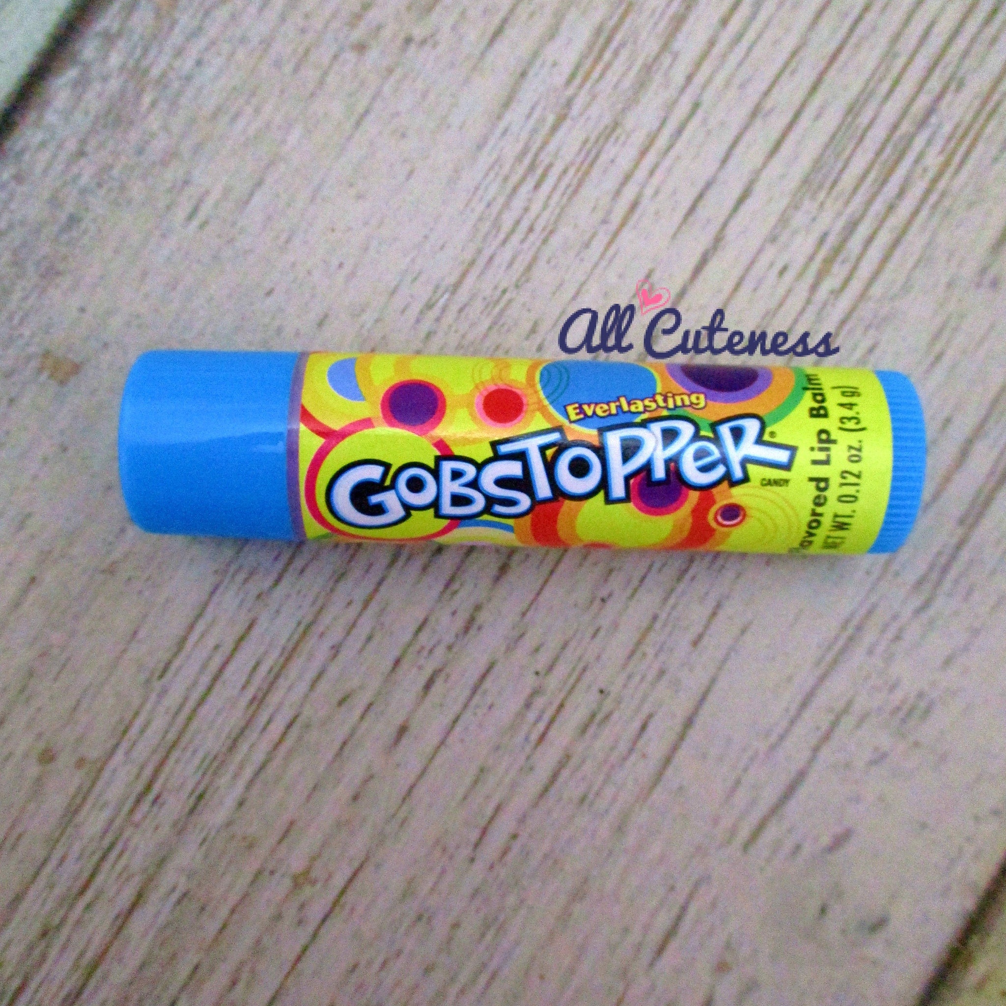 Lip balm tube with blue, yellow, and purple pattern, "GOBSTOPPER" text visible on wooden surface