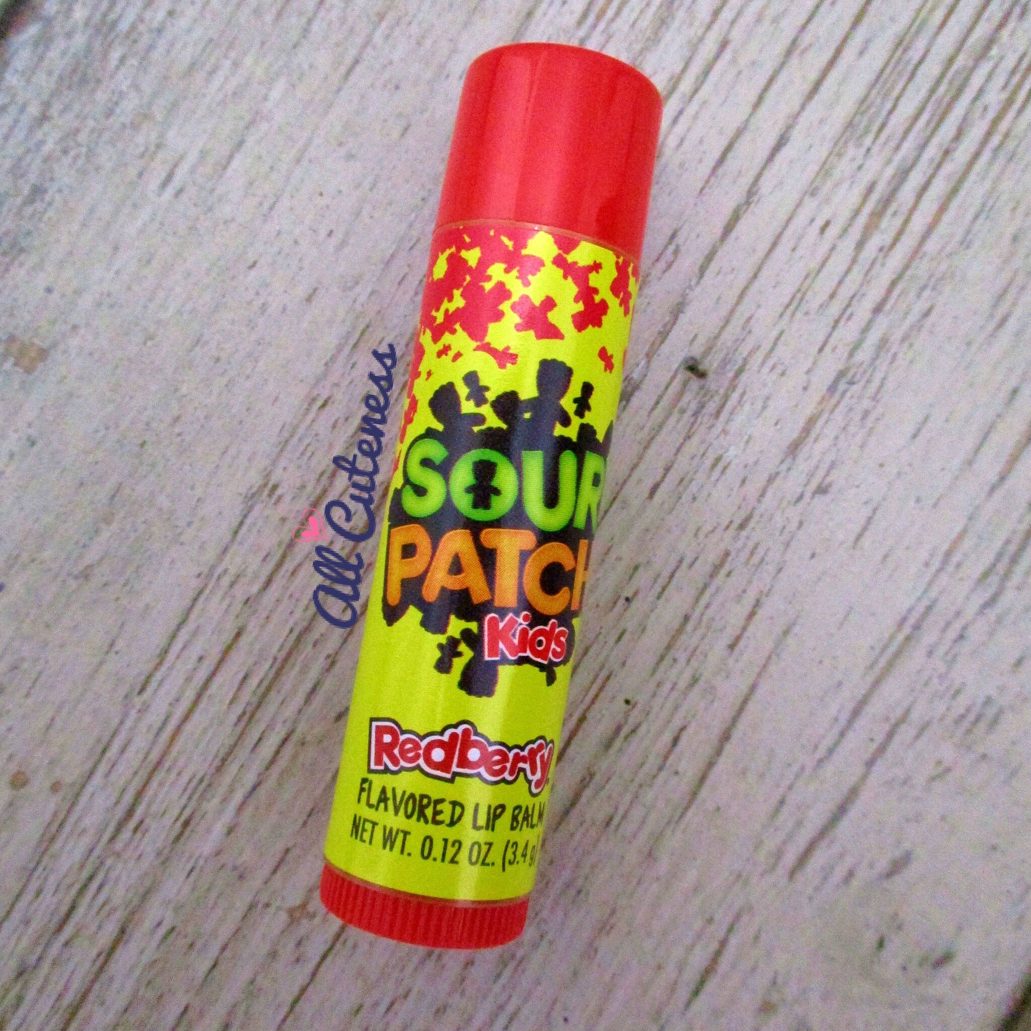 Lip balm tube with red and yellow colors, Sour Patch Kids branding, and flavored text shown.