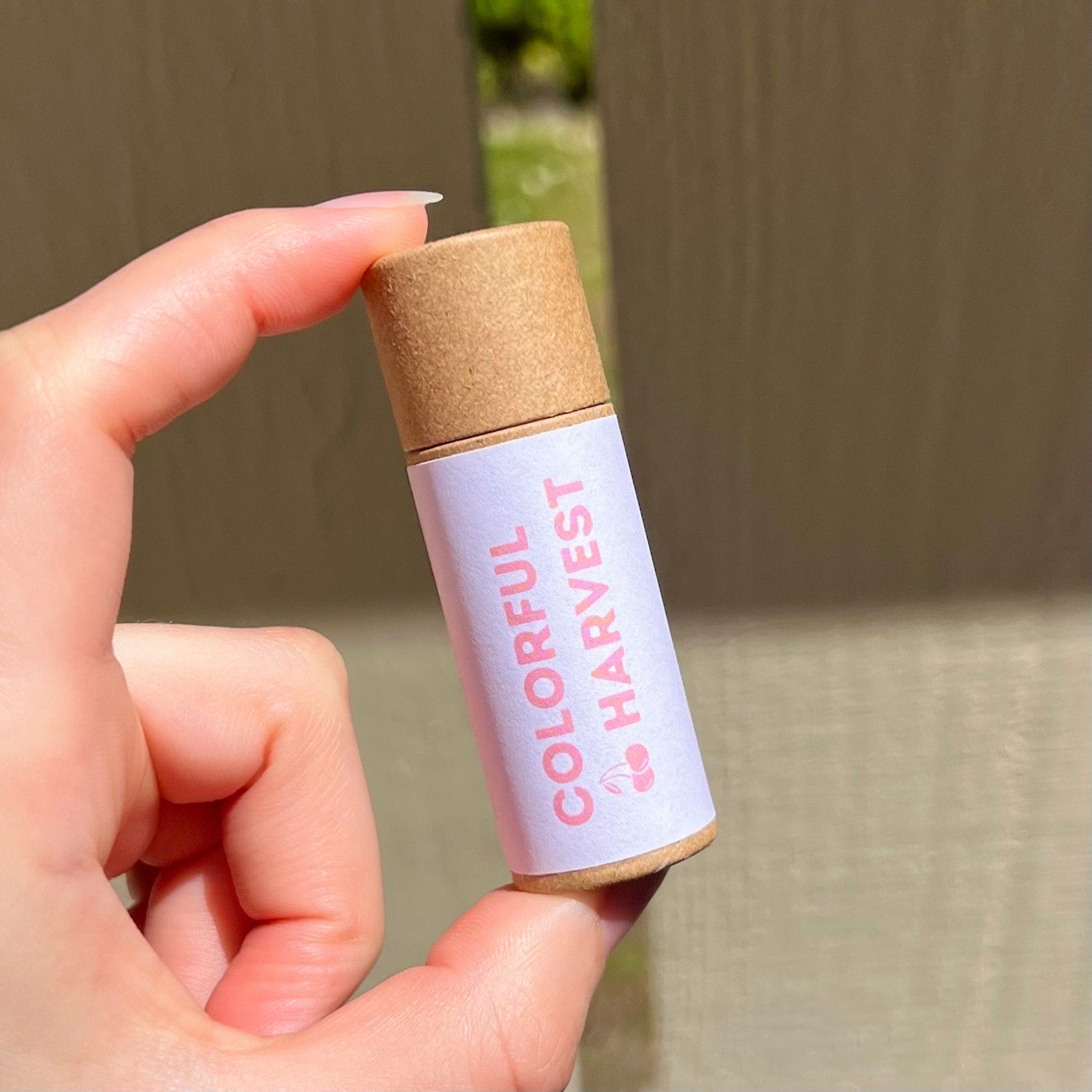 Lip balm tube with brown cap, white label, and "Colorful Harvest" text, held in hand