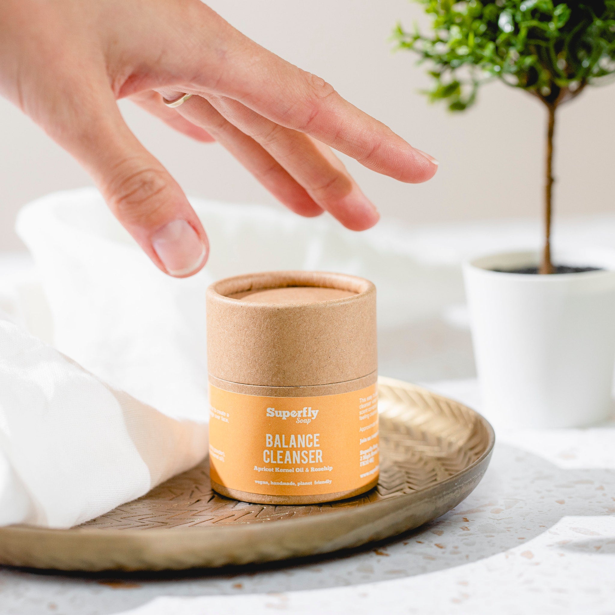 Balance cleanser cylinder with orange label, brown paper, and hand reaching towards it