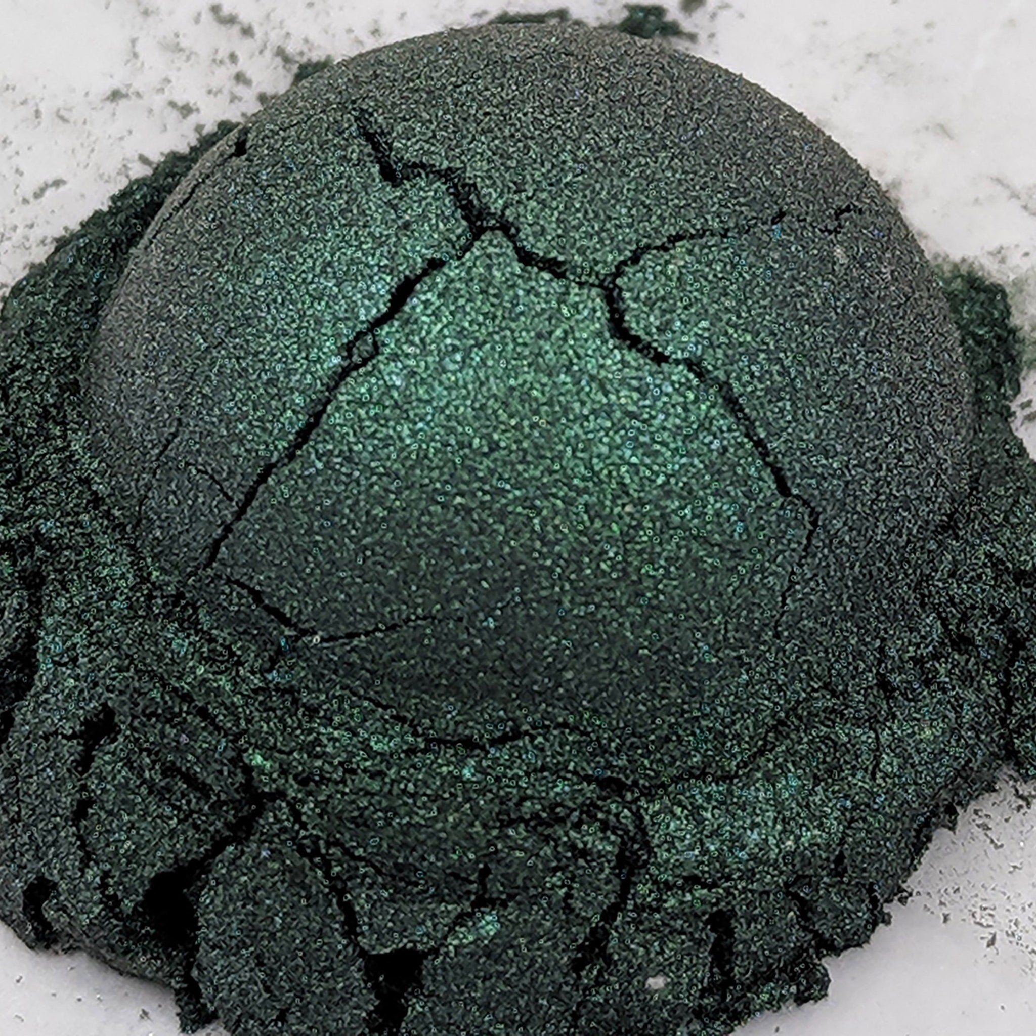 Side view of deep emerald green shimmer loose powder eyeshadow with duochrome effect in open jar