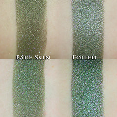 Hand applying vegan loose powder eye shadow in dark olive green with pink sparkle to eyelid