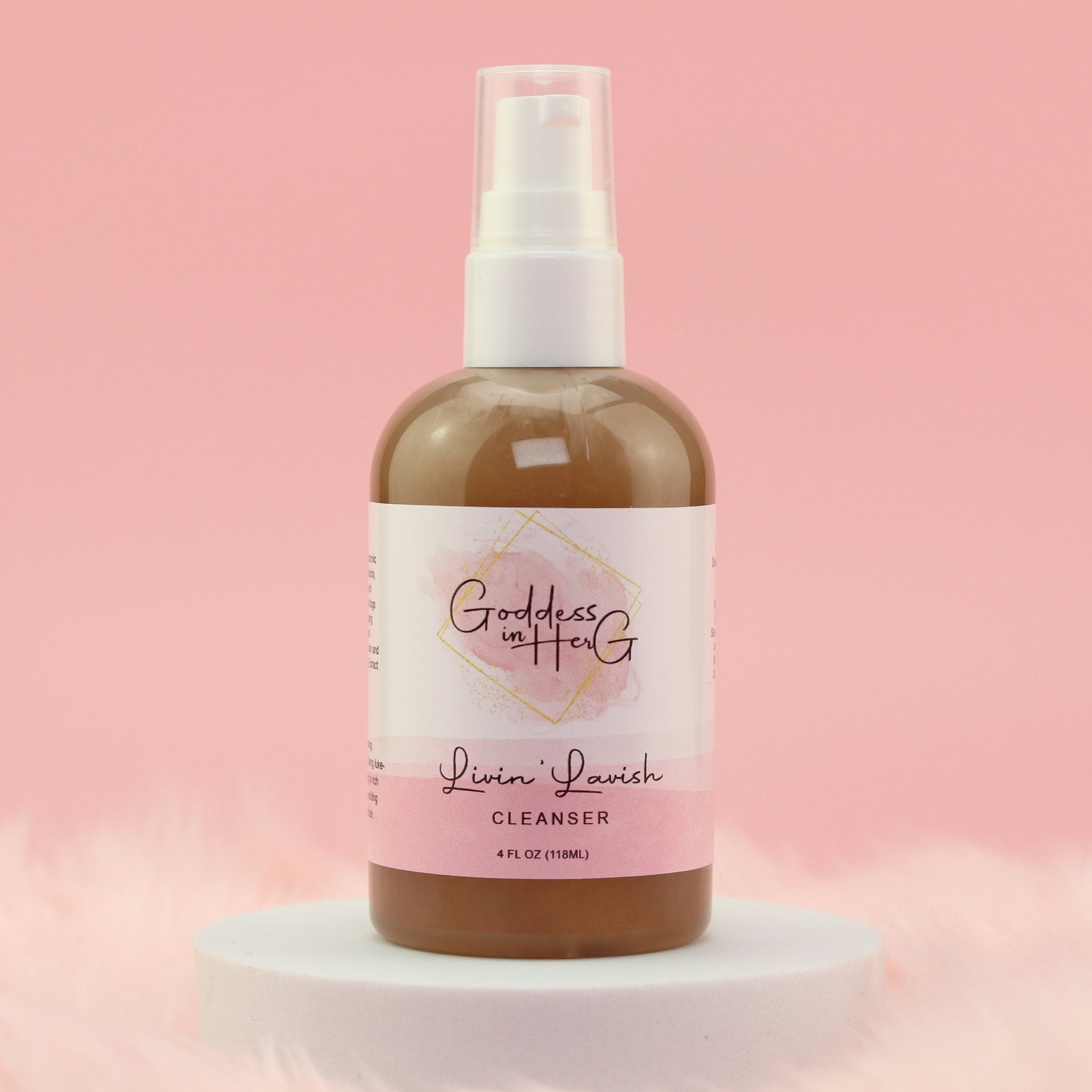 Cleanser bottle with white pump, brown liquid, and pink label with "Goddess in Her G" text on a white pedestal