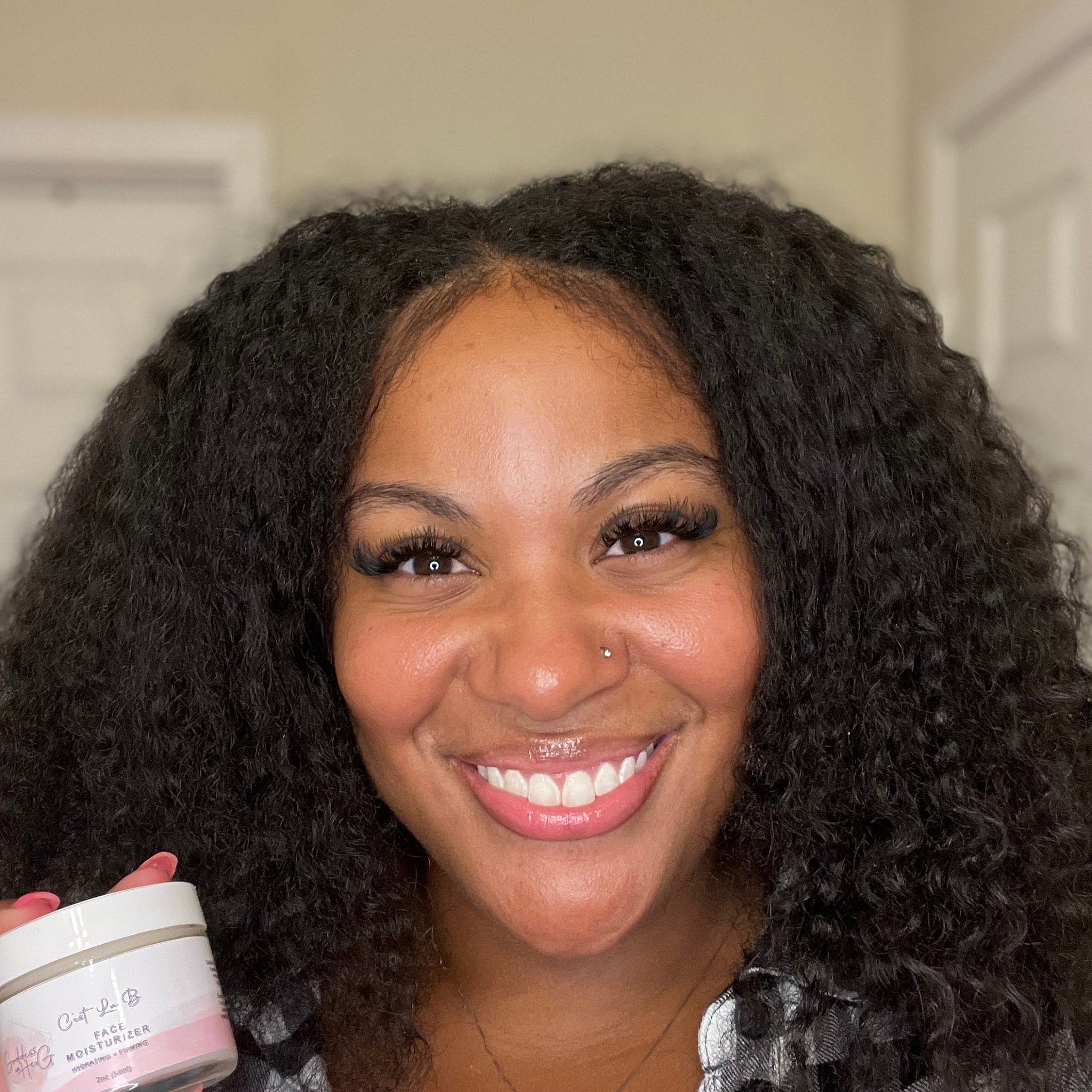 Face moisturizer jar with white and pink label, held by smiling woman with dark curly hair
