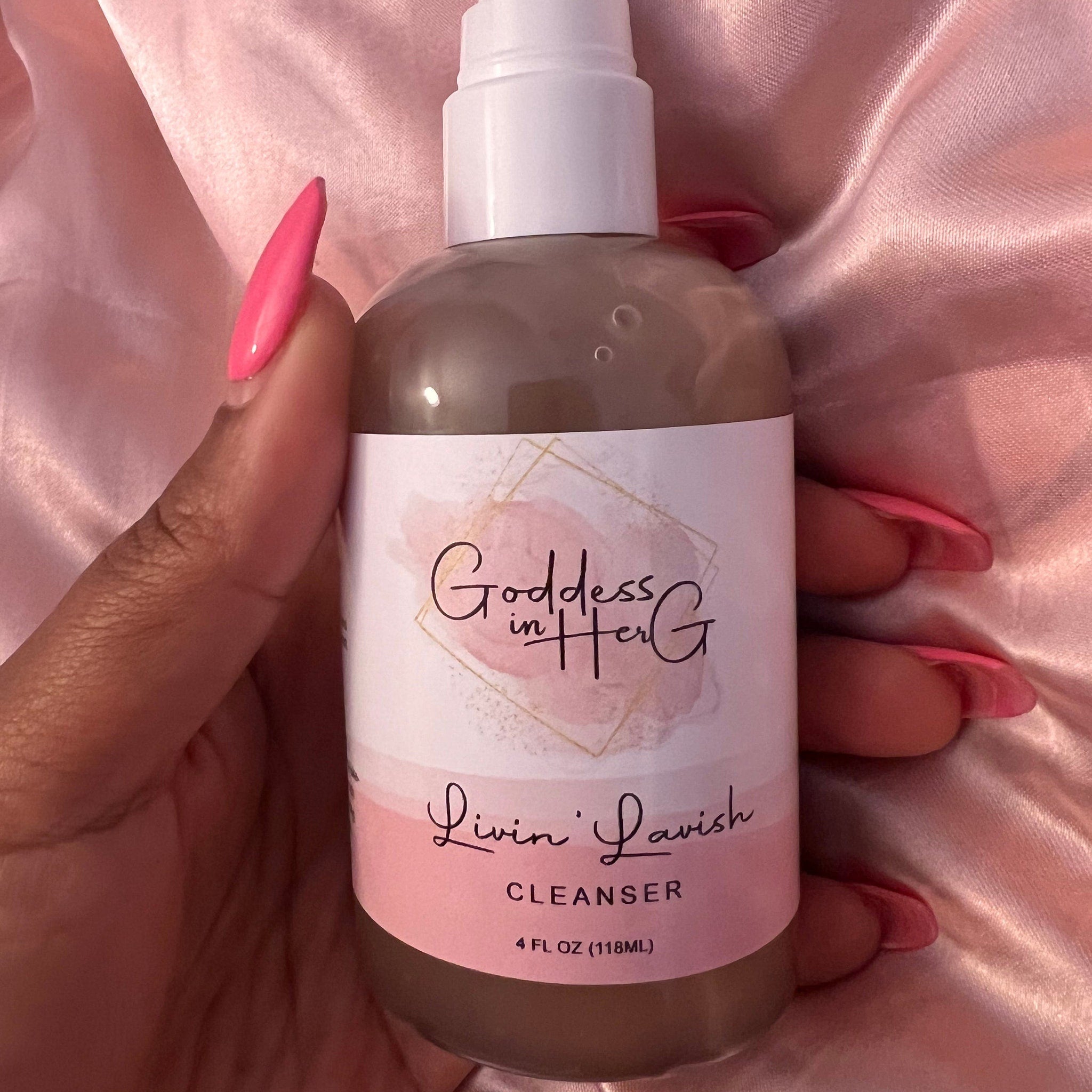Cleanser bottle with white cap, pink and white label, held by hand with pink nails on pink satin fabric