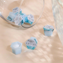 Powder wash pods in blue and white with Suisai branding, scattered near a glass container