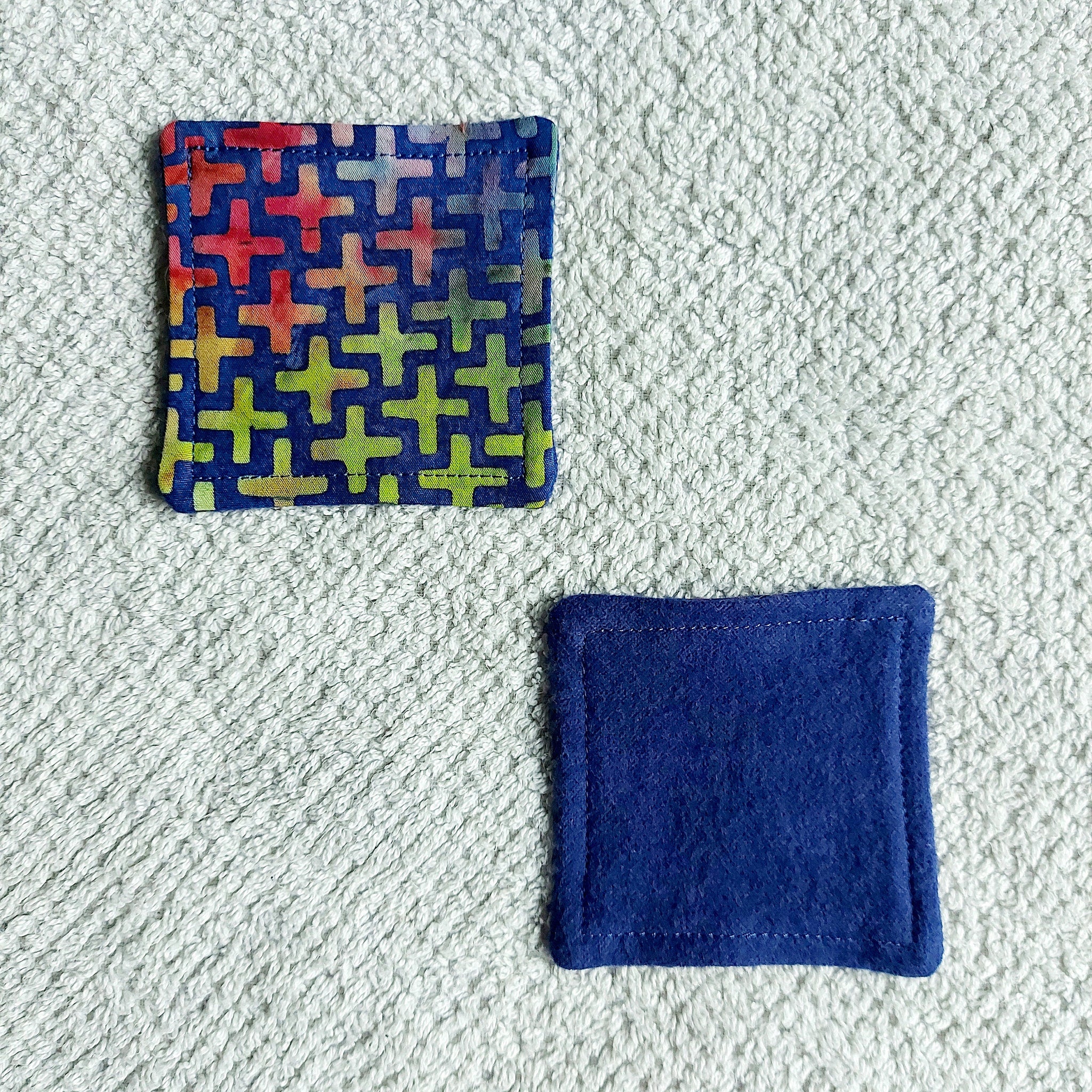Coaster set with colorful plus pattern, blue felt, and stitched edges on textured surface