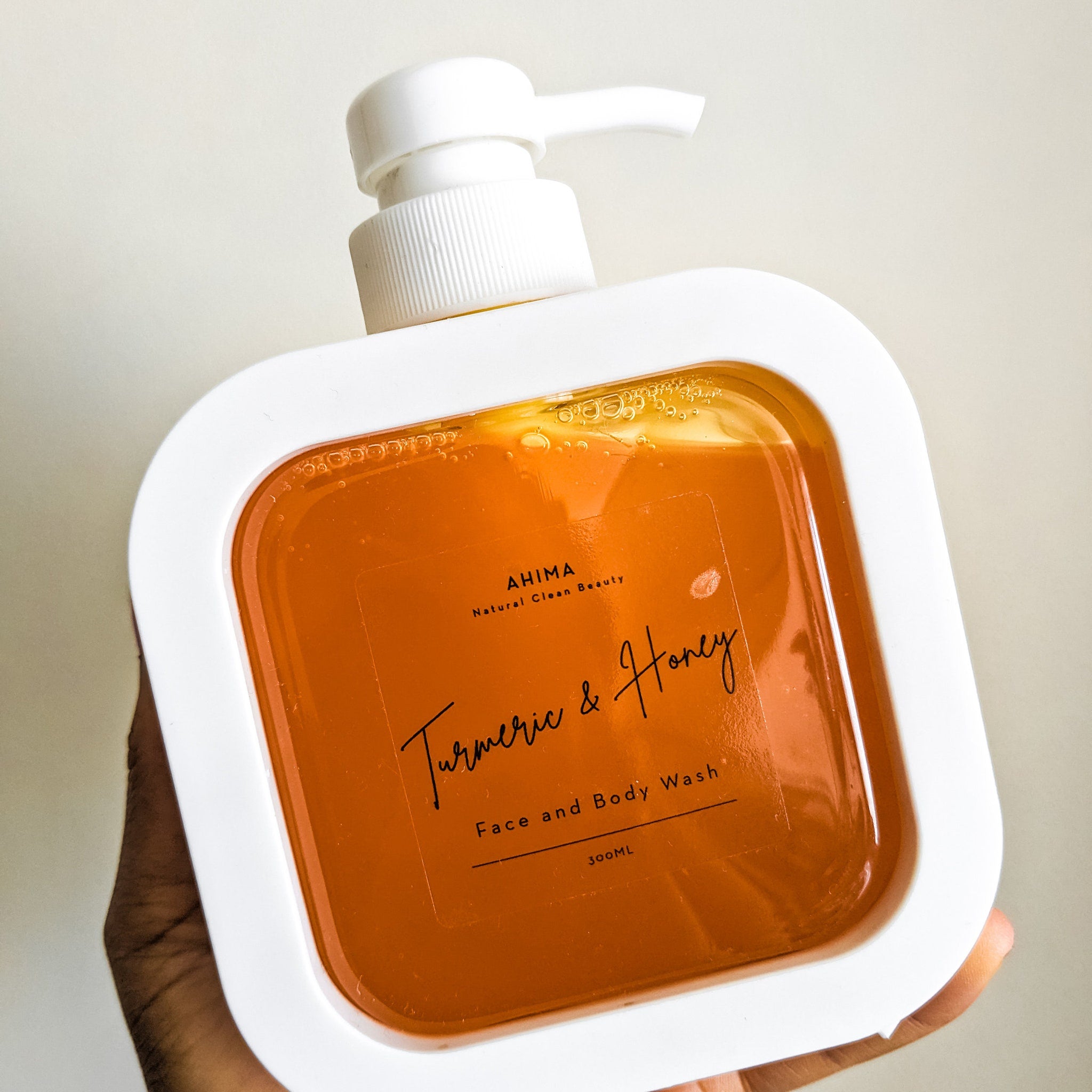 Face and body wash bottle with white frame, orange liquid, and AHIMA label