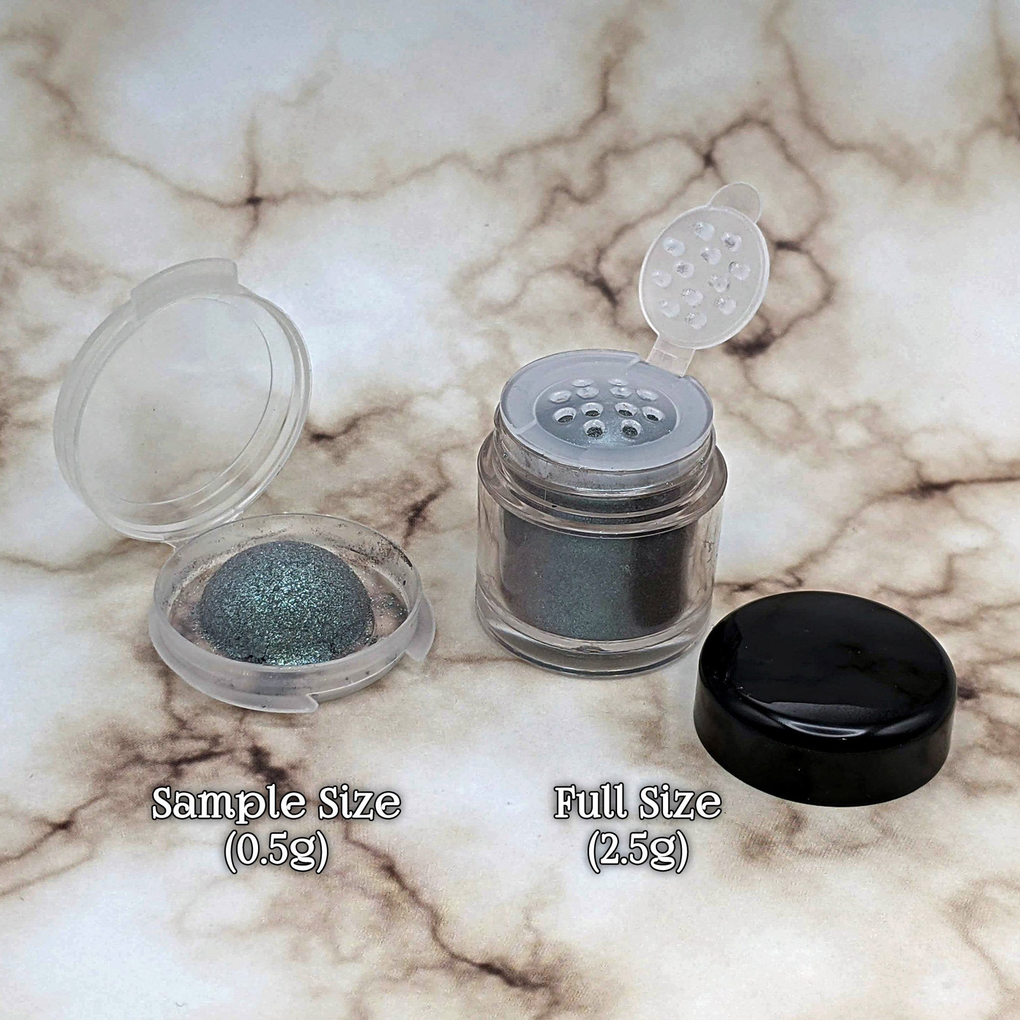 Eyeshadow samples in clear and black containers with metallic green pigment, marble background