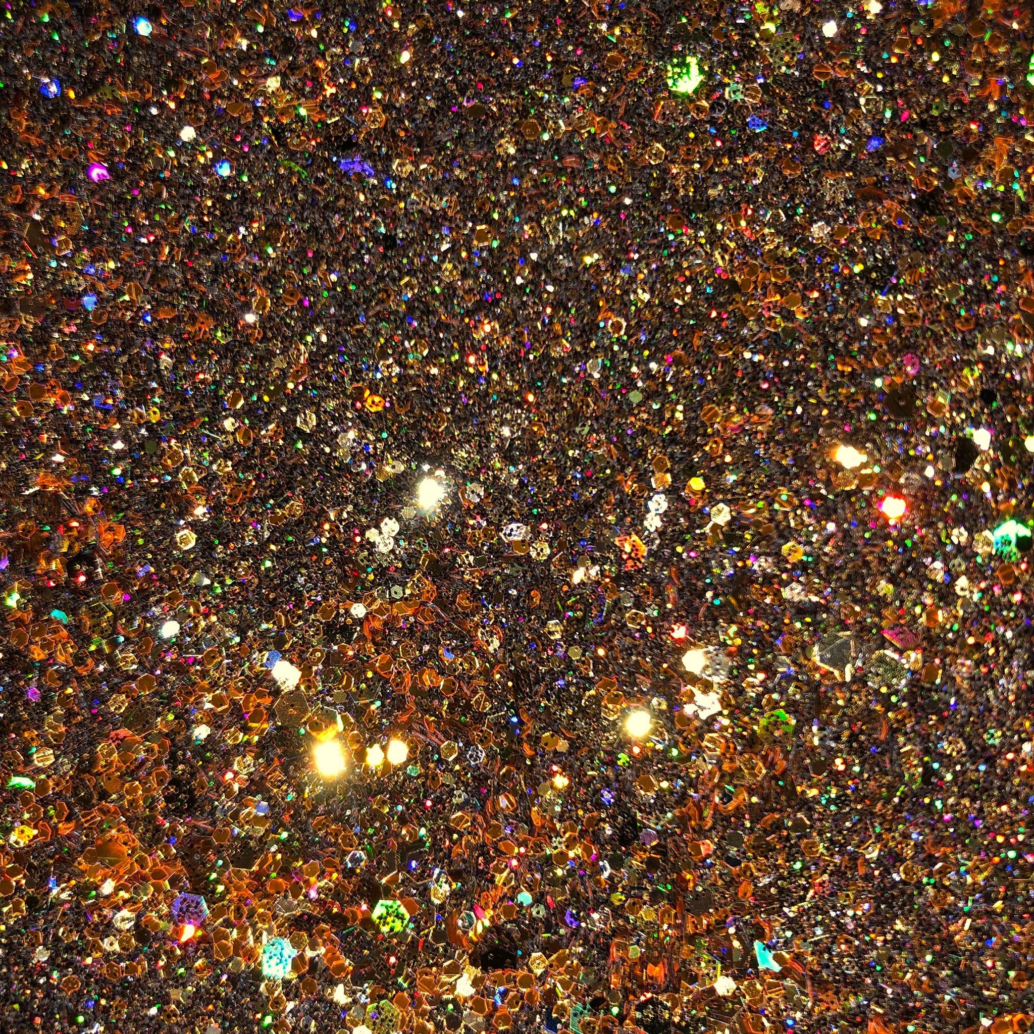 Close-up of warm brown glitter eyeshadow with intense gold shimmer particles in pressed powder pan