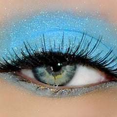 Close-up of fingertips applying shimmering peach eye shadow to eyelid with soft blending brush