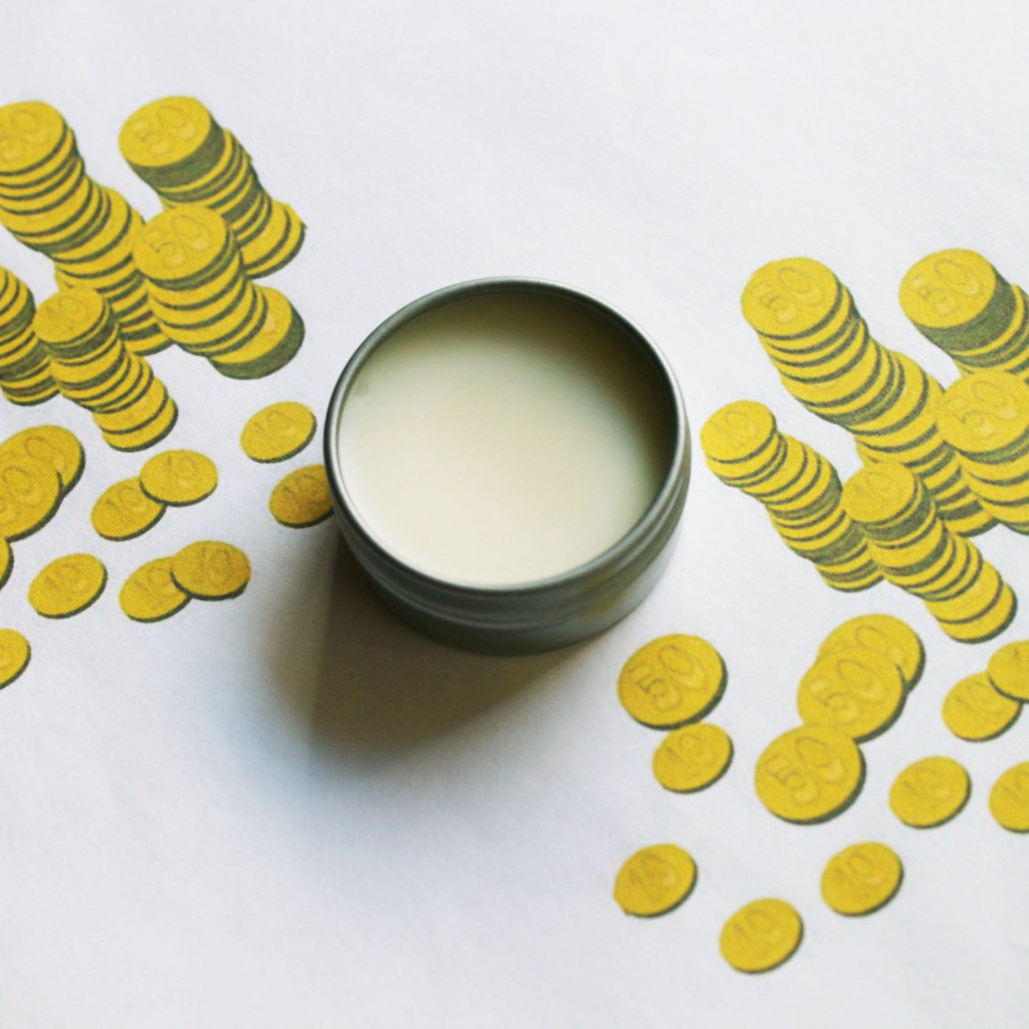 Lip balm in metal tin with white balm, surrounded by yellow coin illustrations on white background