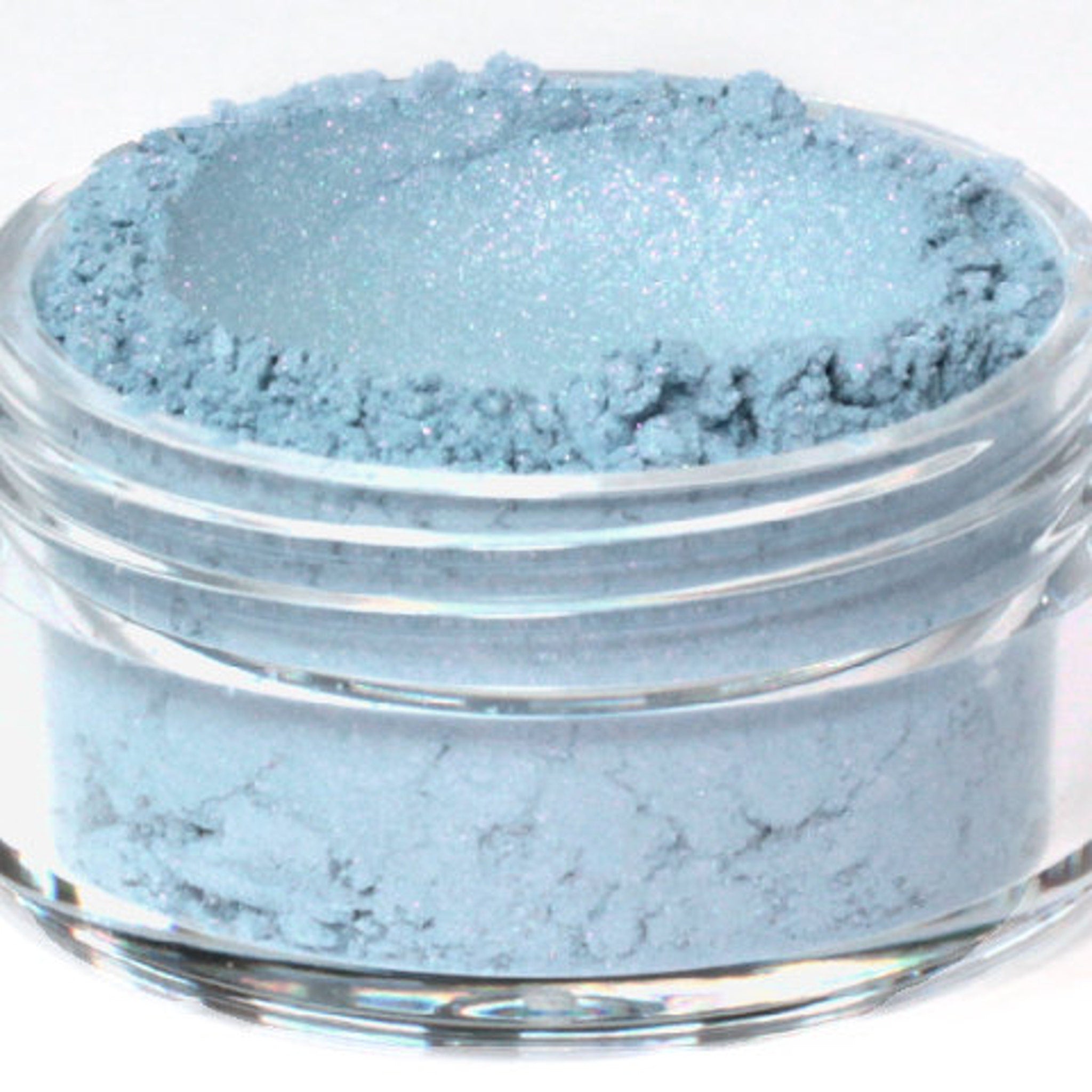 Close-up of vegan mineral eyeshadow in shimmering blue with pink and turquoise flecks, showcasing texture.