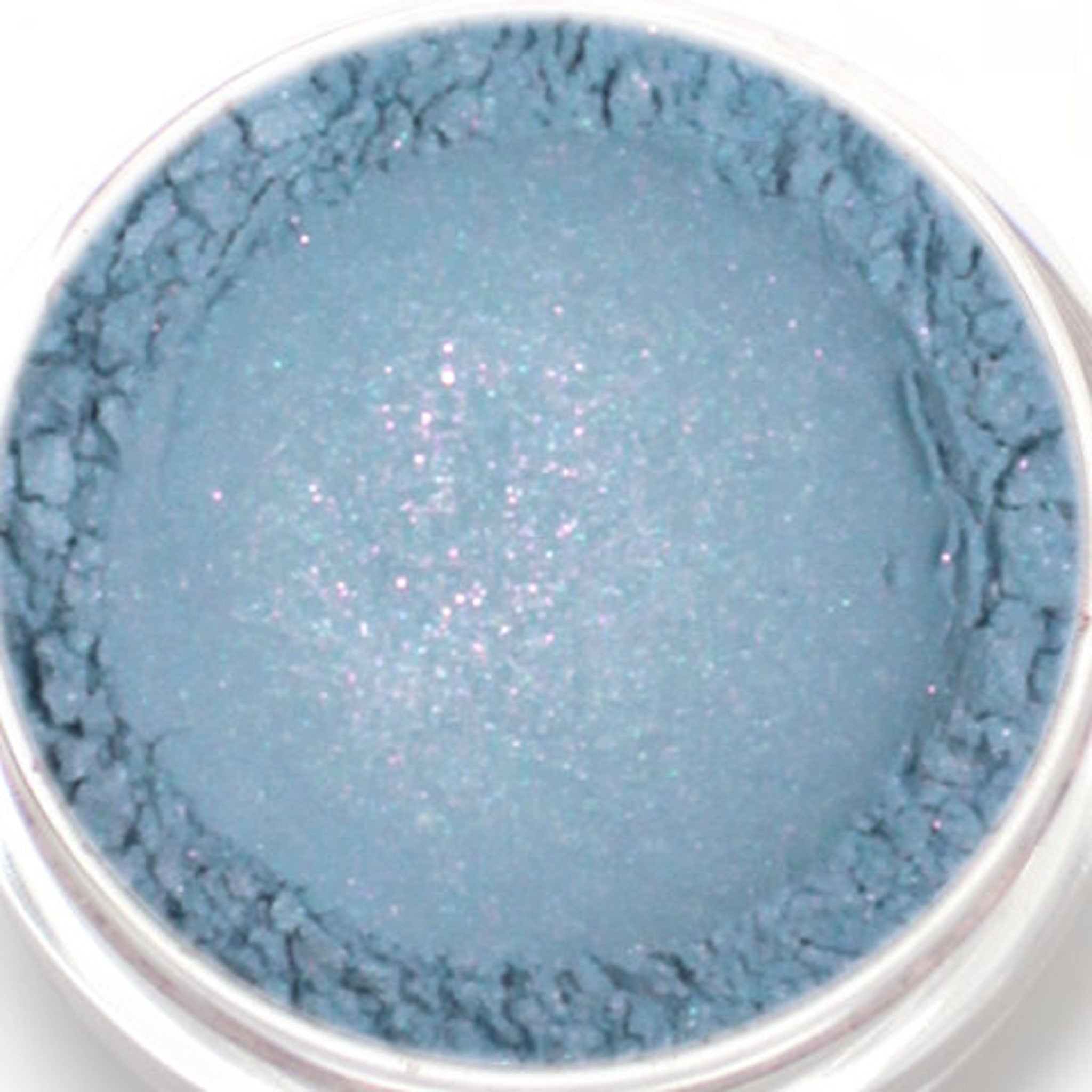 Blue eyeshadow powder with shimmer and textured edges in a clear container