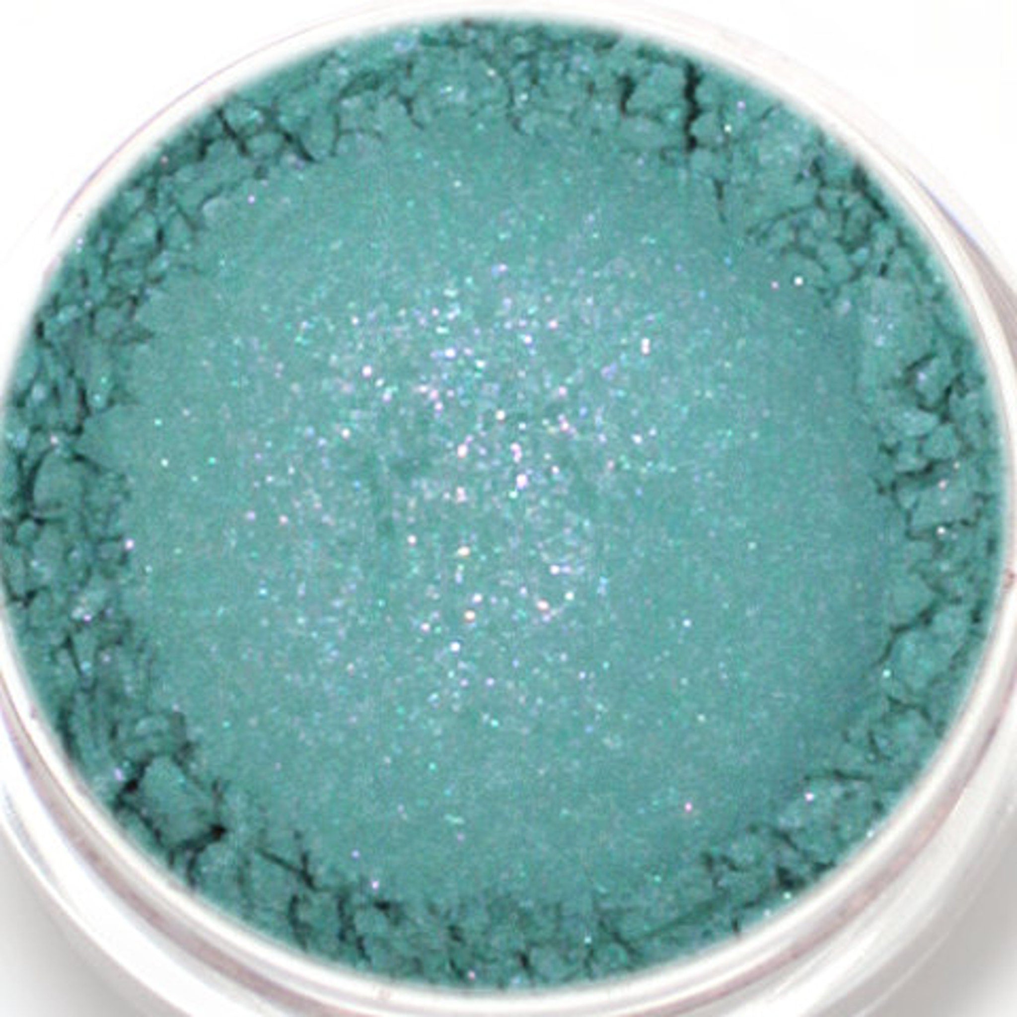 Side view of vegan mineral eyeshadow pot showing blue base with vibrant purple duochrome shift in natural light