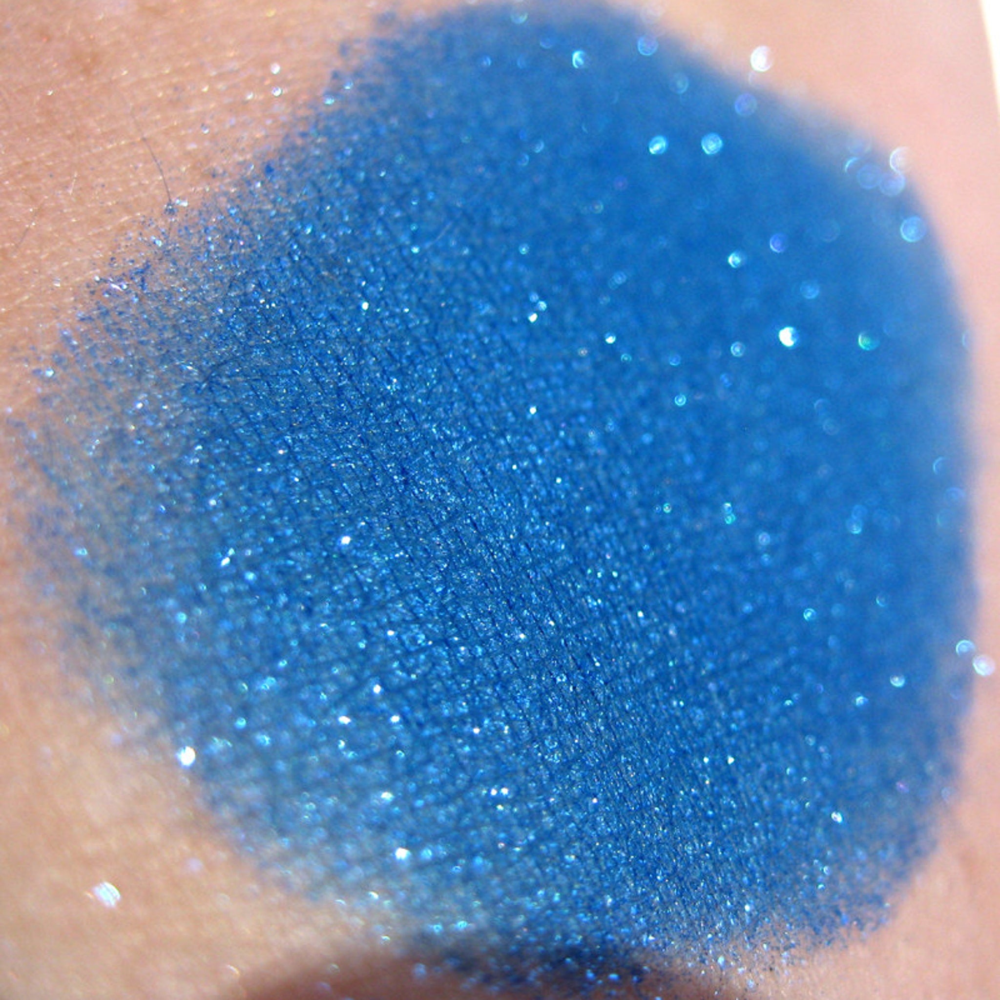 Side view of royal blue loose mineral eyeshadow with iridescent turquoise shimmer and glitter particles catching light.