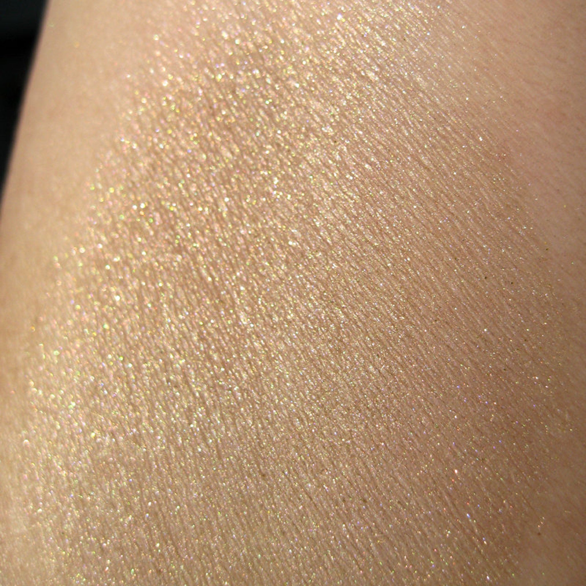 Side view of loose mineral eyeshadow in sheer tan with gold and green pearl shimmer, showcasing silky texture