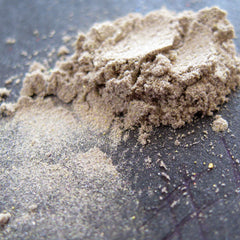 Side view of loose mineral eyeshadow in sheer tan with gold and green pearl shimmer, showcasing silky texture