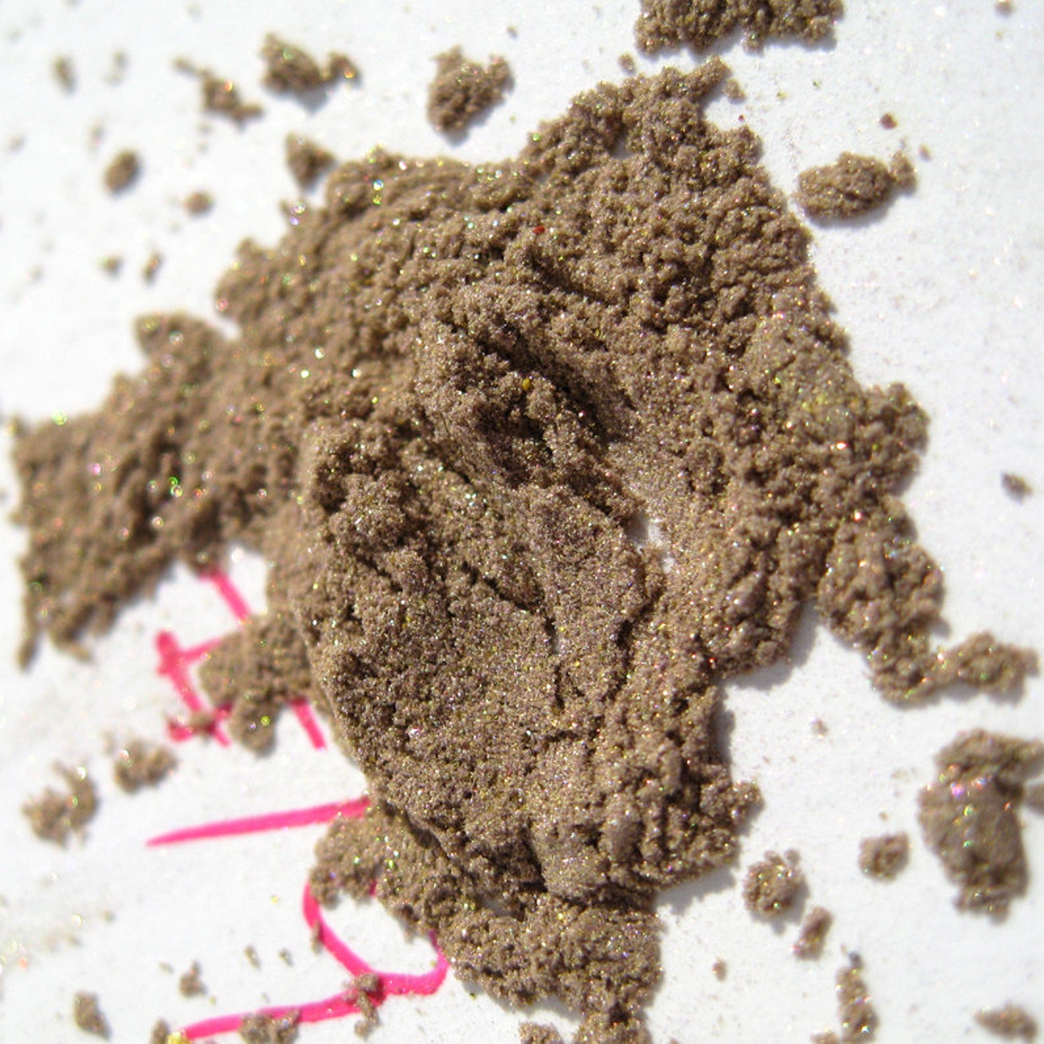 Close-up of loose mineral eyeshadow in neutral taupe beige with gold and green shimmer, showcasing silky texture