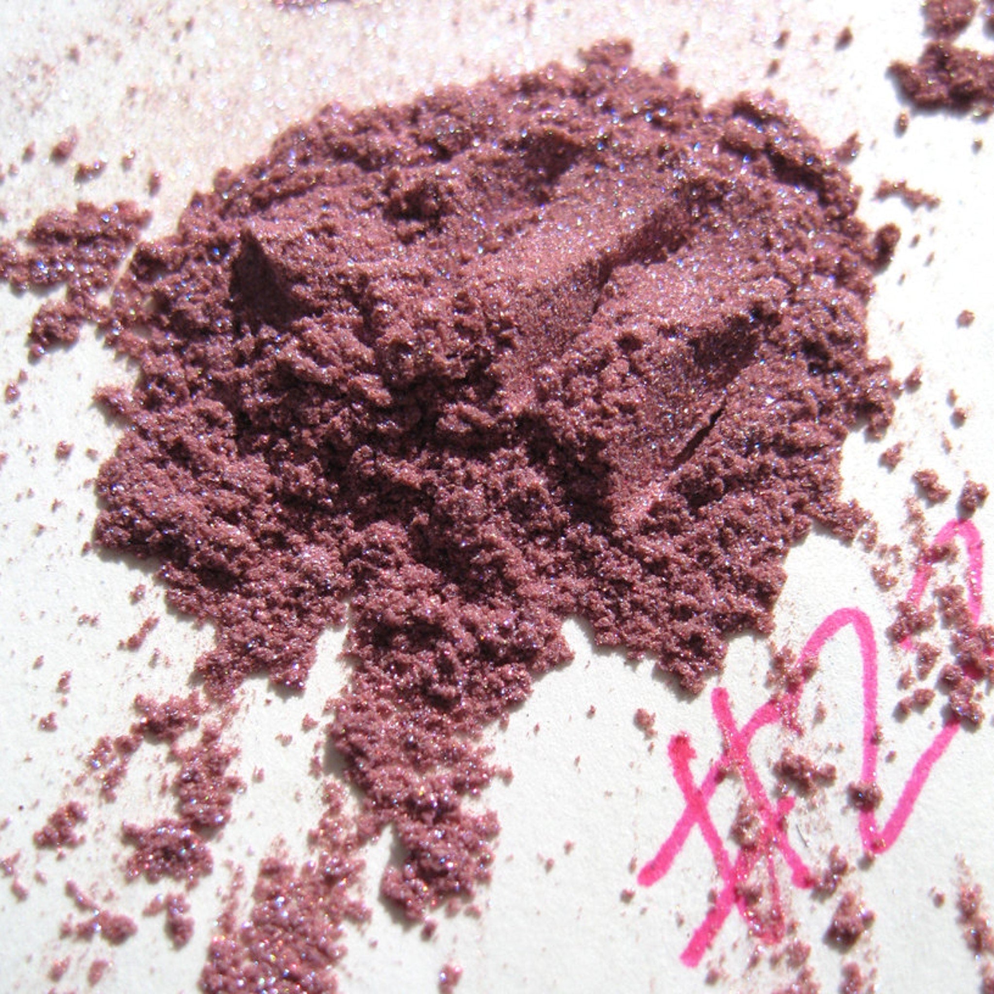 Powdered eyeshadow in mauve with glitter and pink markings on white background