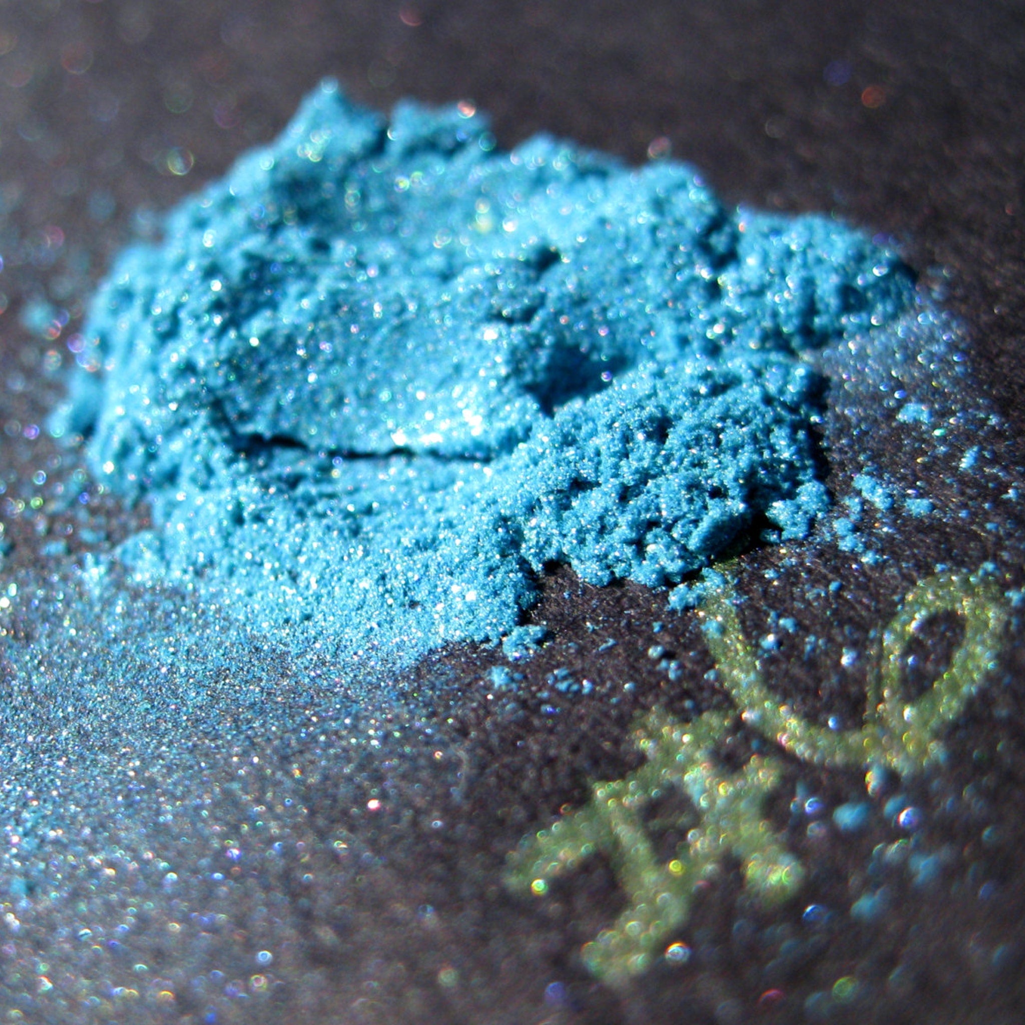 Side view of loose turquoise blue eye shadow with teal, iridescent aqua, and purple shimmer in mineral pigment jar