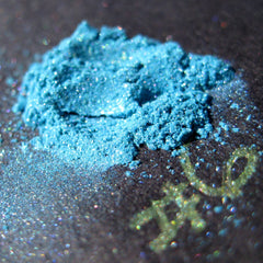 Side view of loose turquoise blue eye shadow with teal, iridescent aqua, and purple shimmer in mineral pigment jar