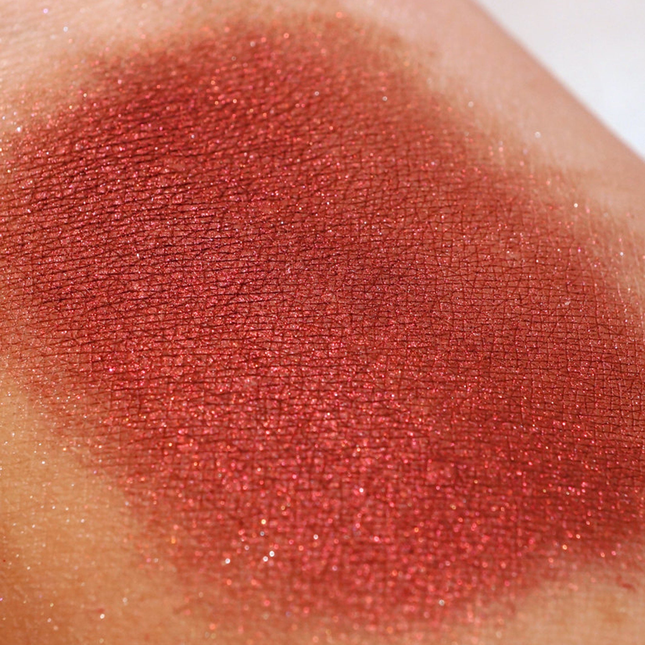 Side view of Bloodflower loose mineral eyeshadow showing metallic blood-red pigment in angled lighting