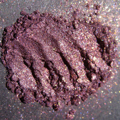 Close-up of warm metallic purple eyeshadow with iridescent copper shimmer and glitter particles in compact.