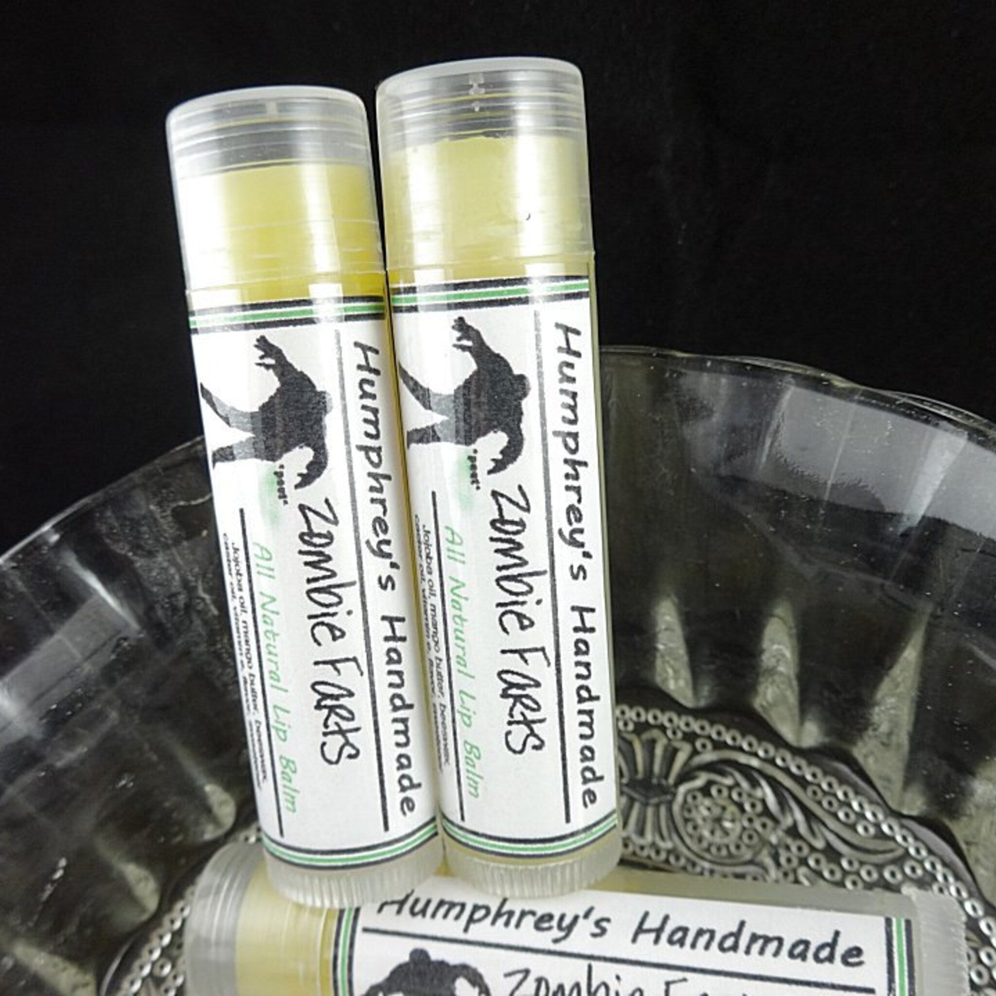 Lip balm tubes with white labels, green stripes, and clear plastic caps; "Humphrey's Handmade Zombie Farts" text visible