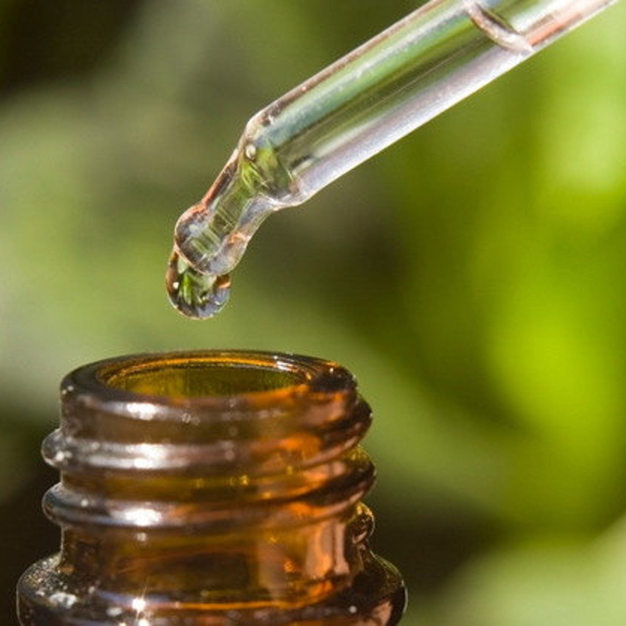 Dropper bottle with amber glass and clear liquid, dispensing a drop of liquid