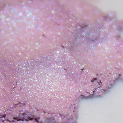 Side view of loose lilac shimmer eyeshadow powder spilling from jar, showcasing pale lavender hue and fine sparkle texture
