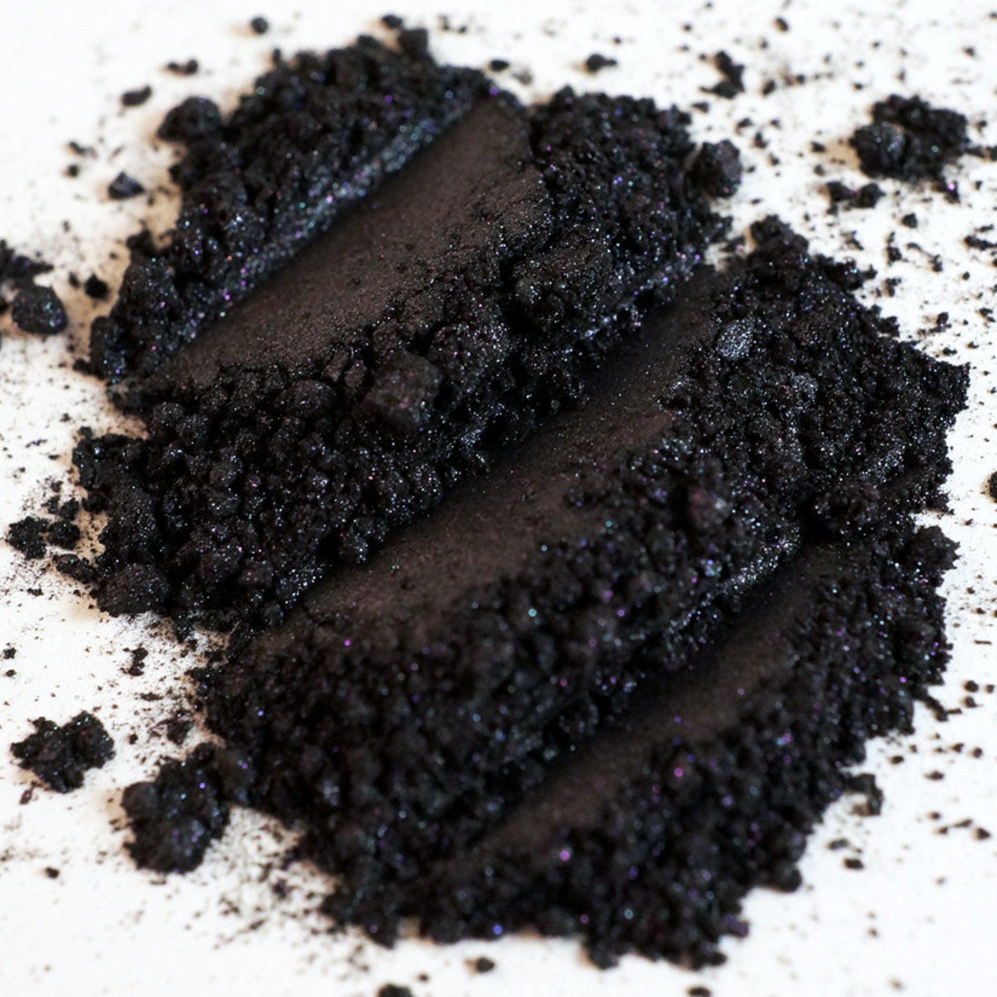 Close-up of iridescent black eyeshadow being applied with a brush, showing metallic gunmetal shimmer on skin