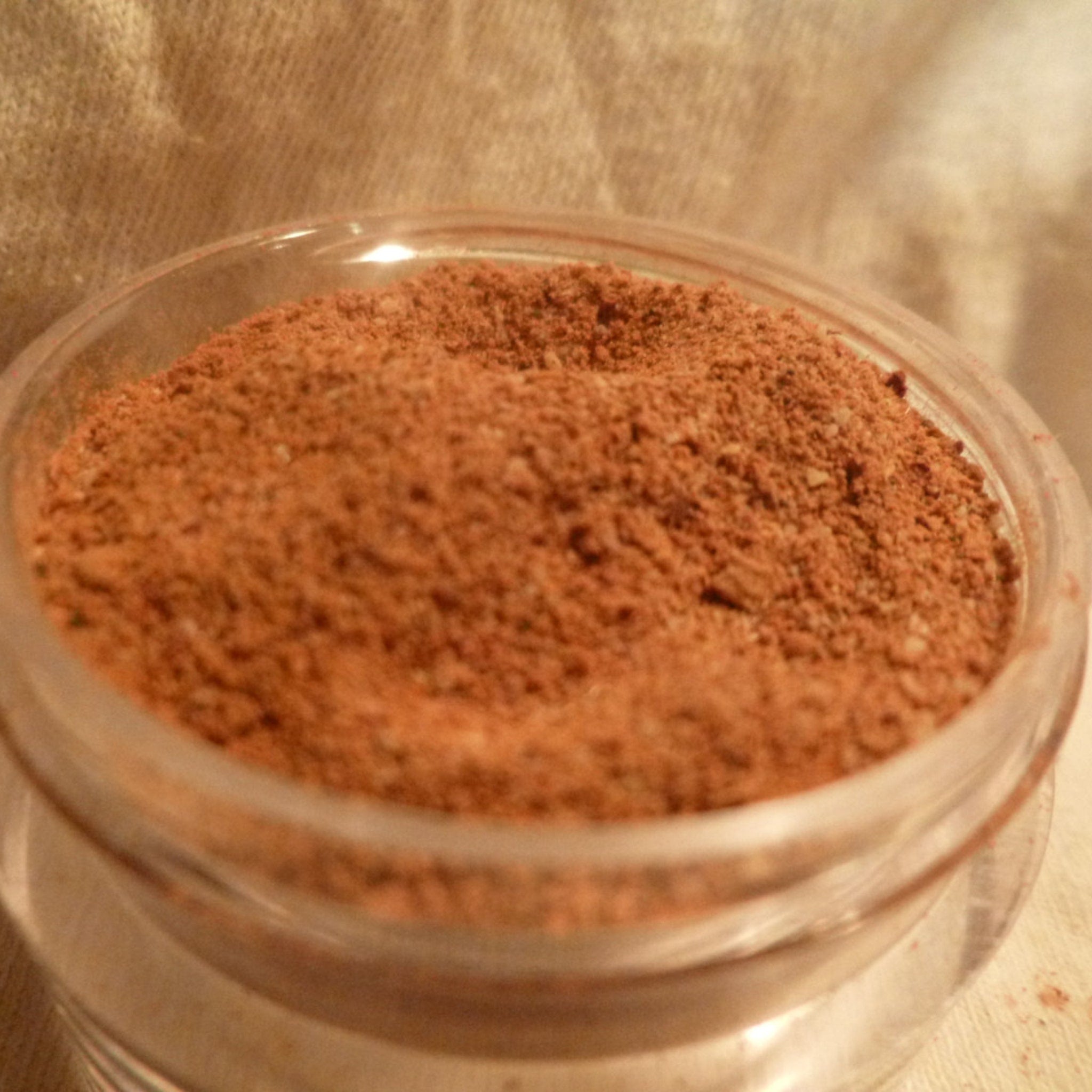 Powdered spice, brown granules in a clear glass container, close-up view