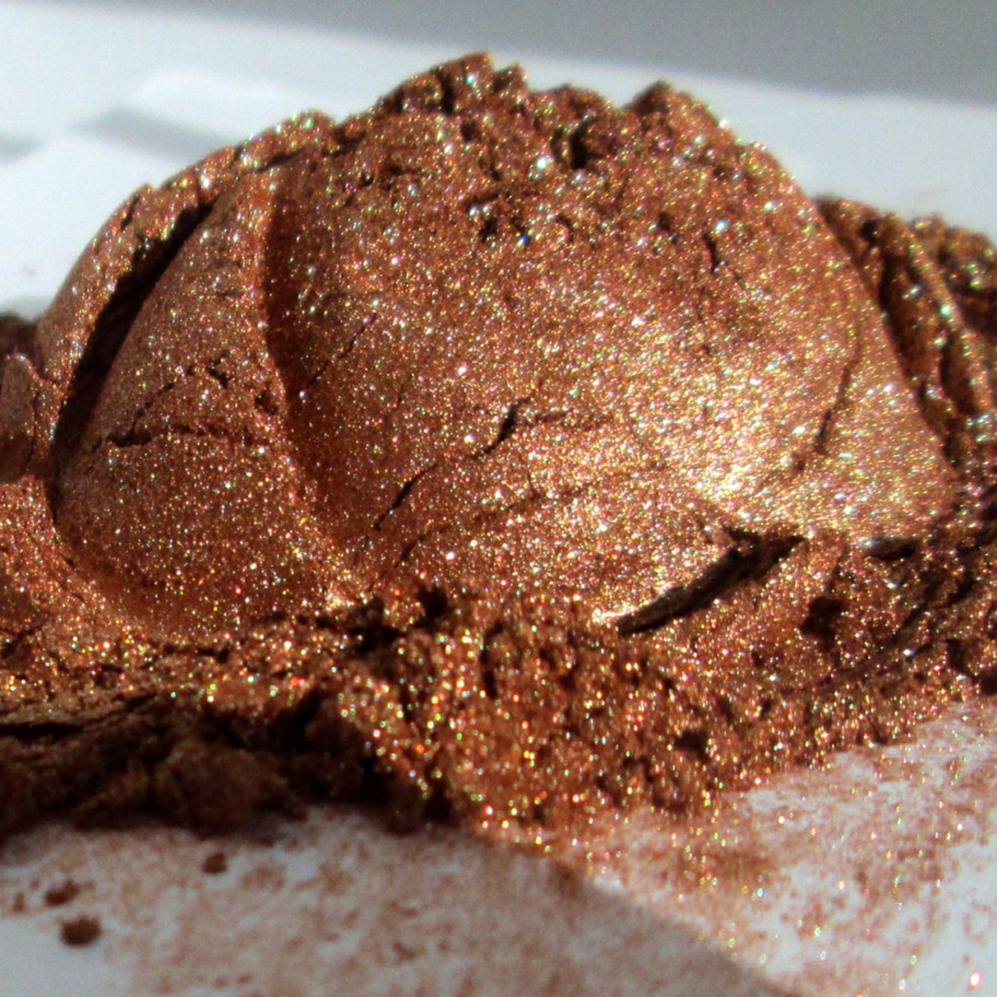 Close-up of bronze and golden mineral eye shadow with shimmering flecks in compact palette