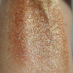 Close-up of fingertips applying bronze and golden mineral eye shadow to eyelid for natural shimmer