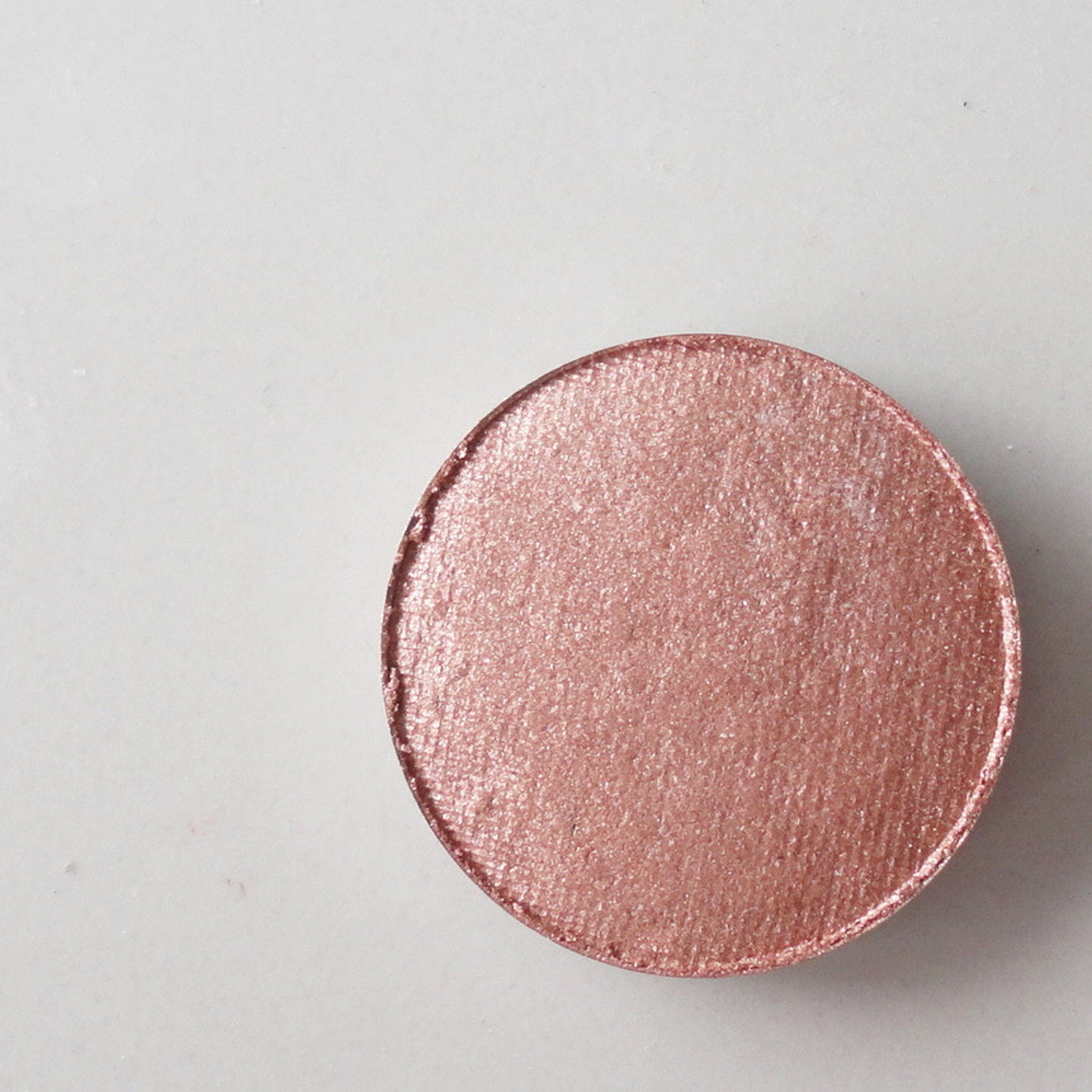 Eyeshadow compact in rose gold shimmer finish, circular shape, on white surface