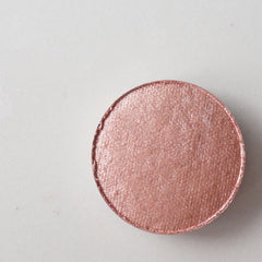 Eyeshadow compact in rose gold shimmer finish, circular shape, on white surface