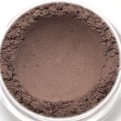 Hand applying deep brown vegan mineral eyeshadow with subtle shimmer to eyelid using a fluffy brush