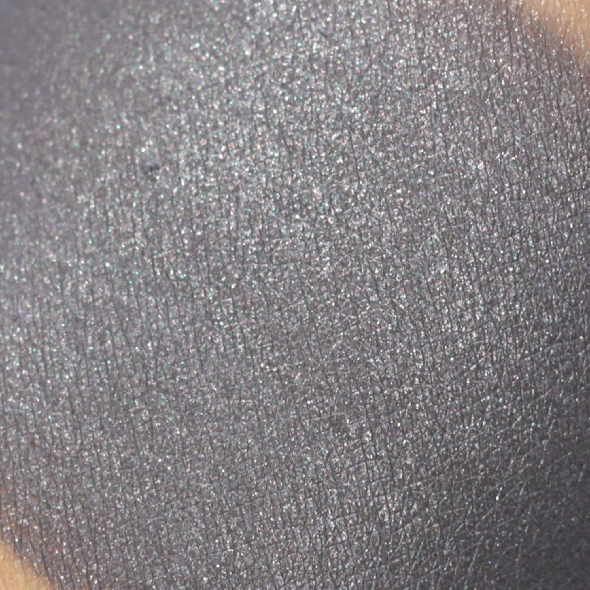Gray eyeshadow swatch with glitter, textured finish, and skin visible