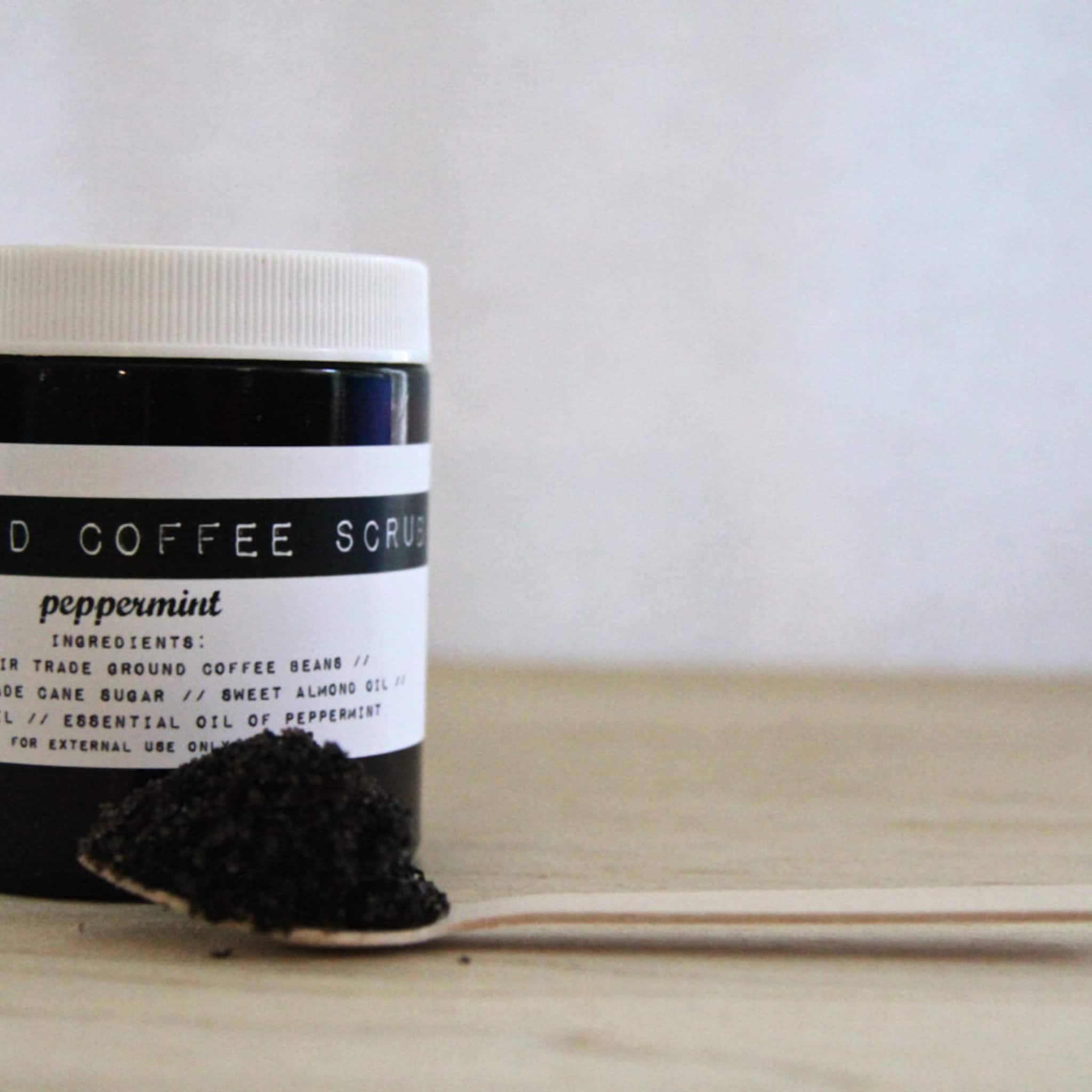 Coffee scrub jar with black and white label, white lid, and dark granules on wooden spoon