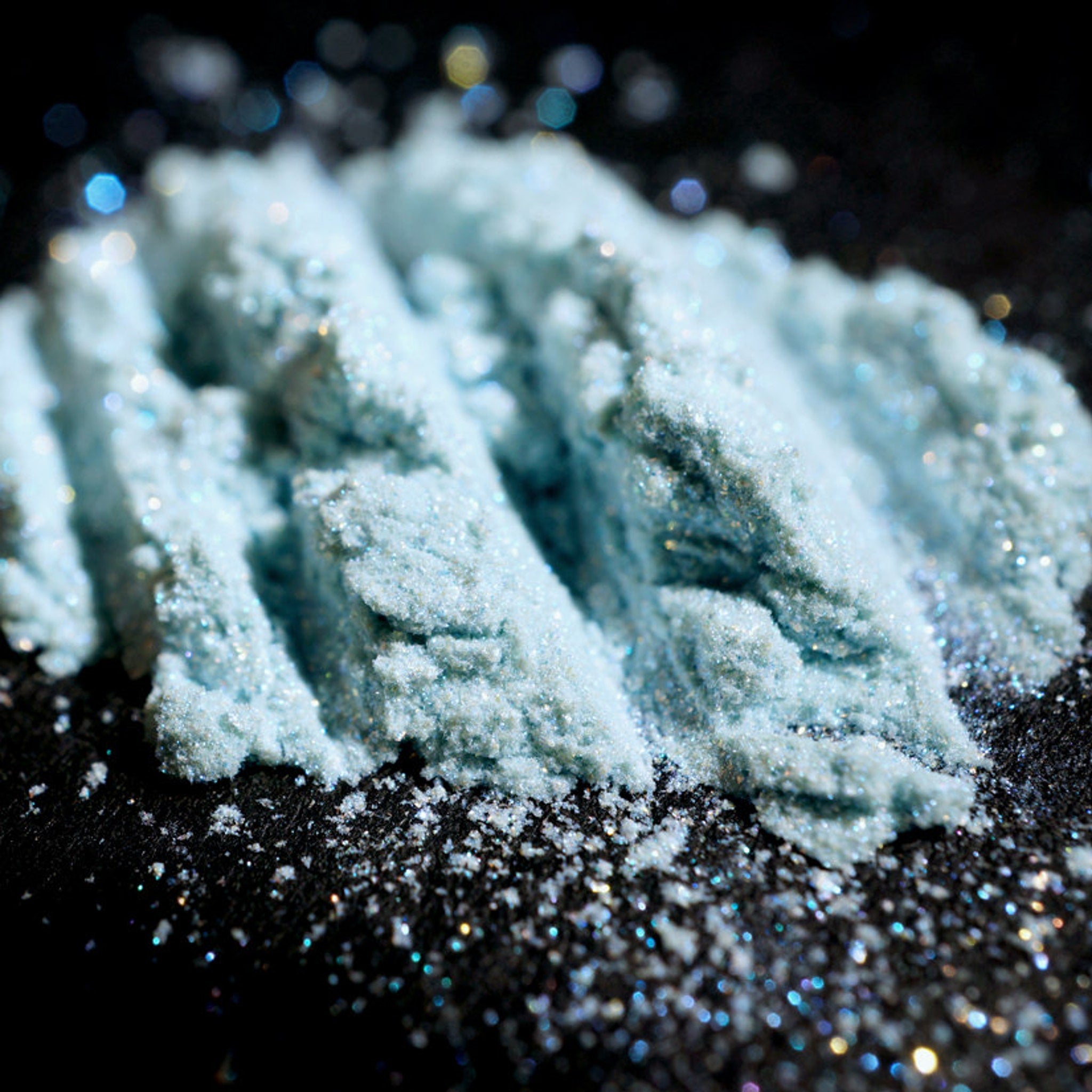 Eye shadow powder, light blue iridescent shimmer, textured lines on dark surface