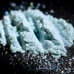 Eye shadow powder, light blue iridescent shimmer, textured lines on dark surface