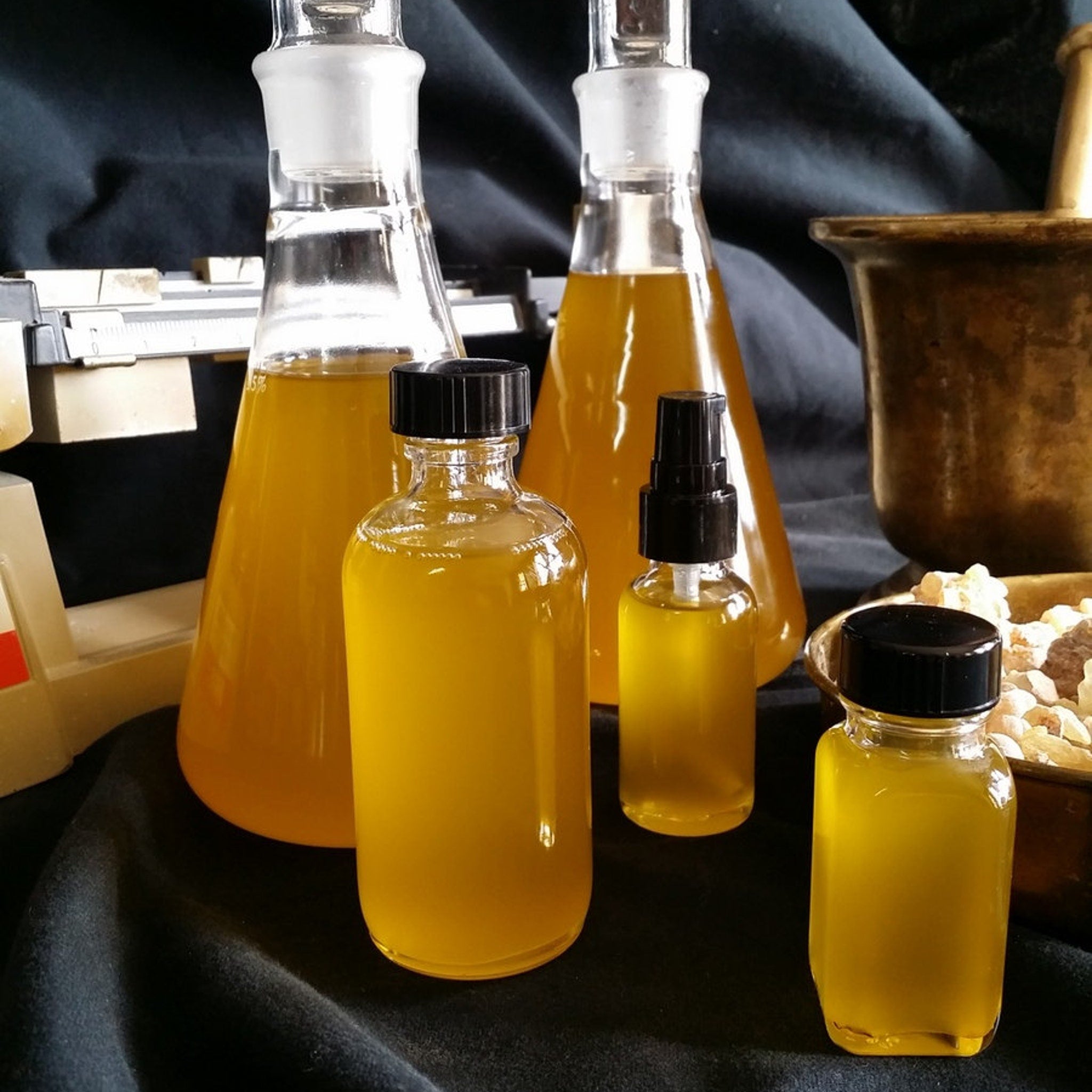 Yellow liquid in glass bottles and flasks with black caps, on dark fabric background